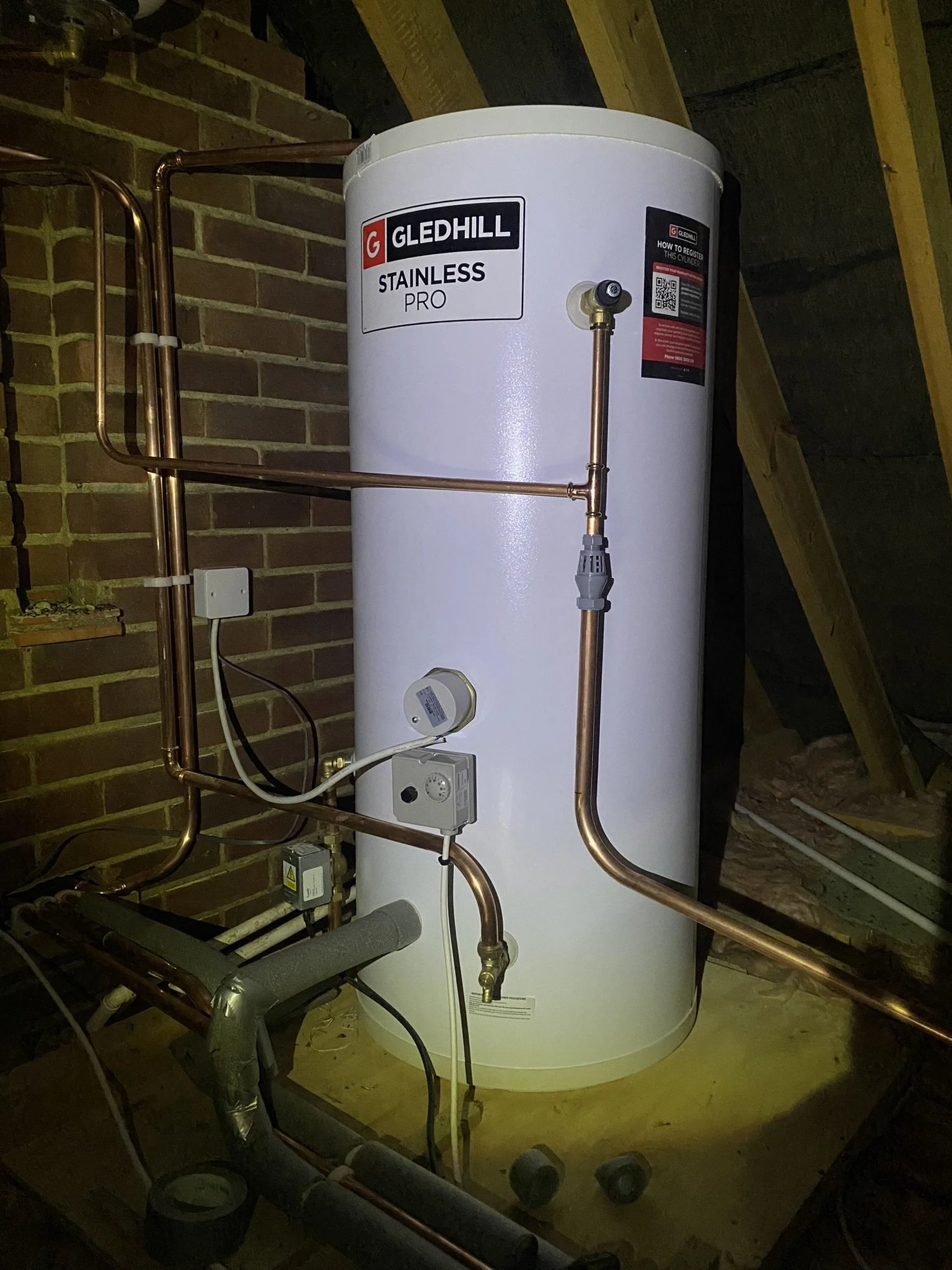 A Gledhill Stainless Pro water heater with copper piping and electrical connections installed in an attic.