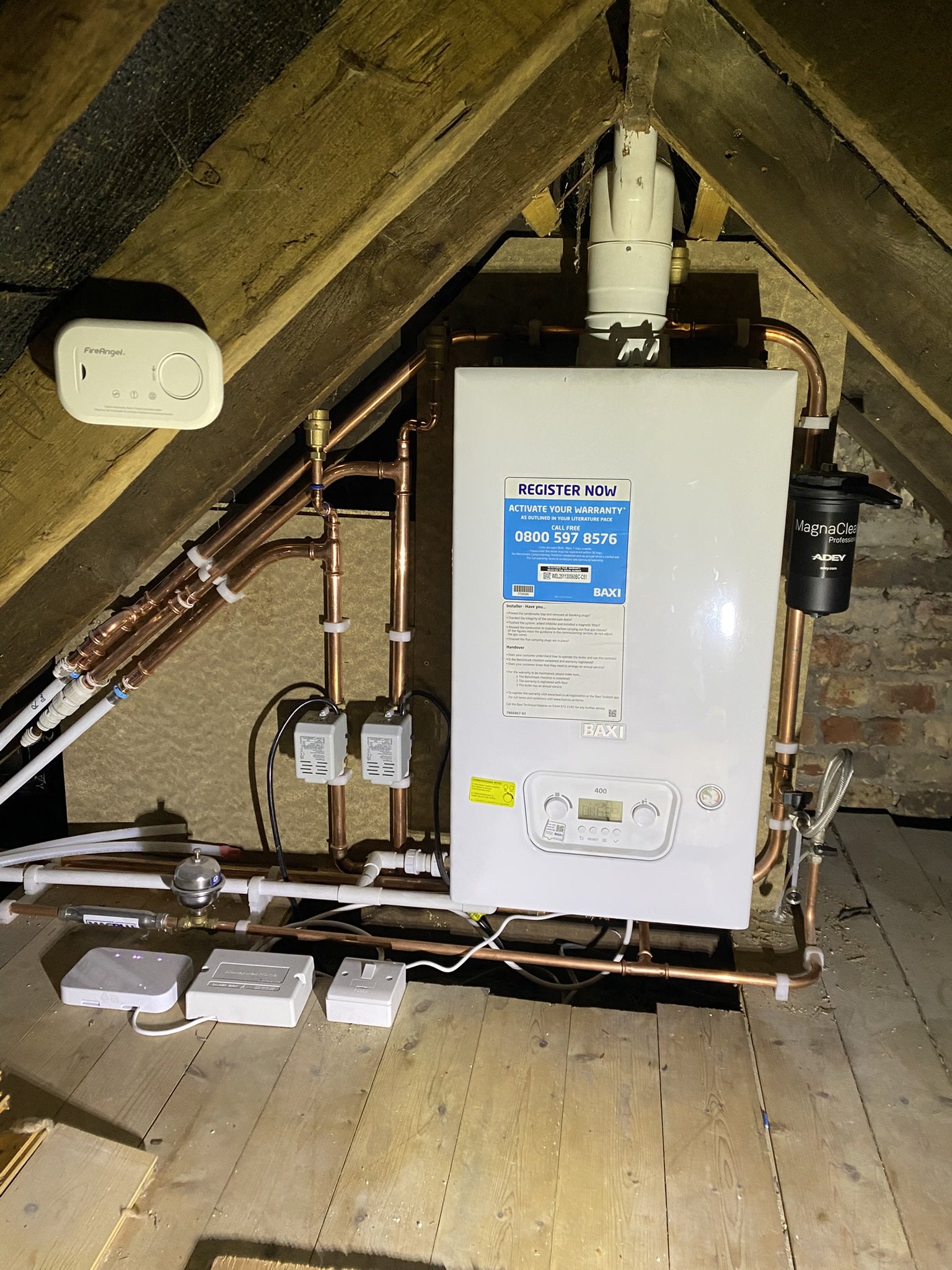 An attic space with a boiler system, copper pipes, and electronic components mounted on the wall and wooden floor.