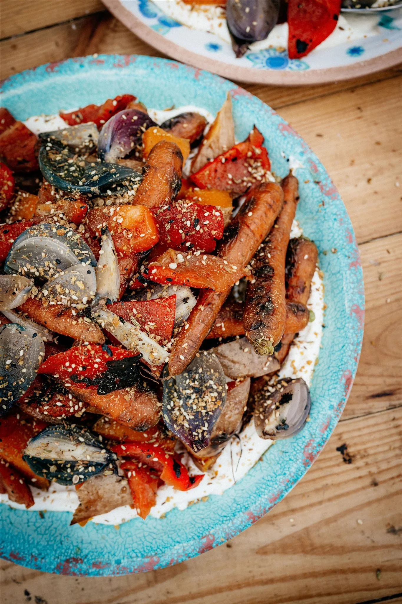 A colorful plate of roasted vegetables and meat with sprinkled sesame seeds, served on a rustic wooden table.