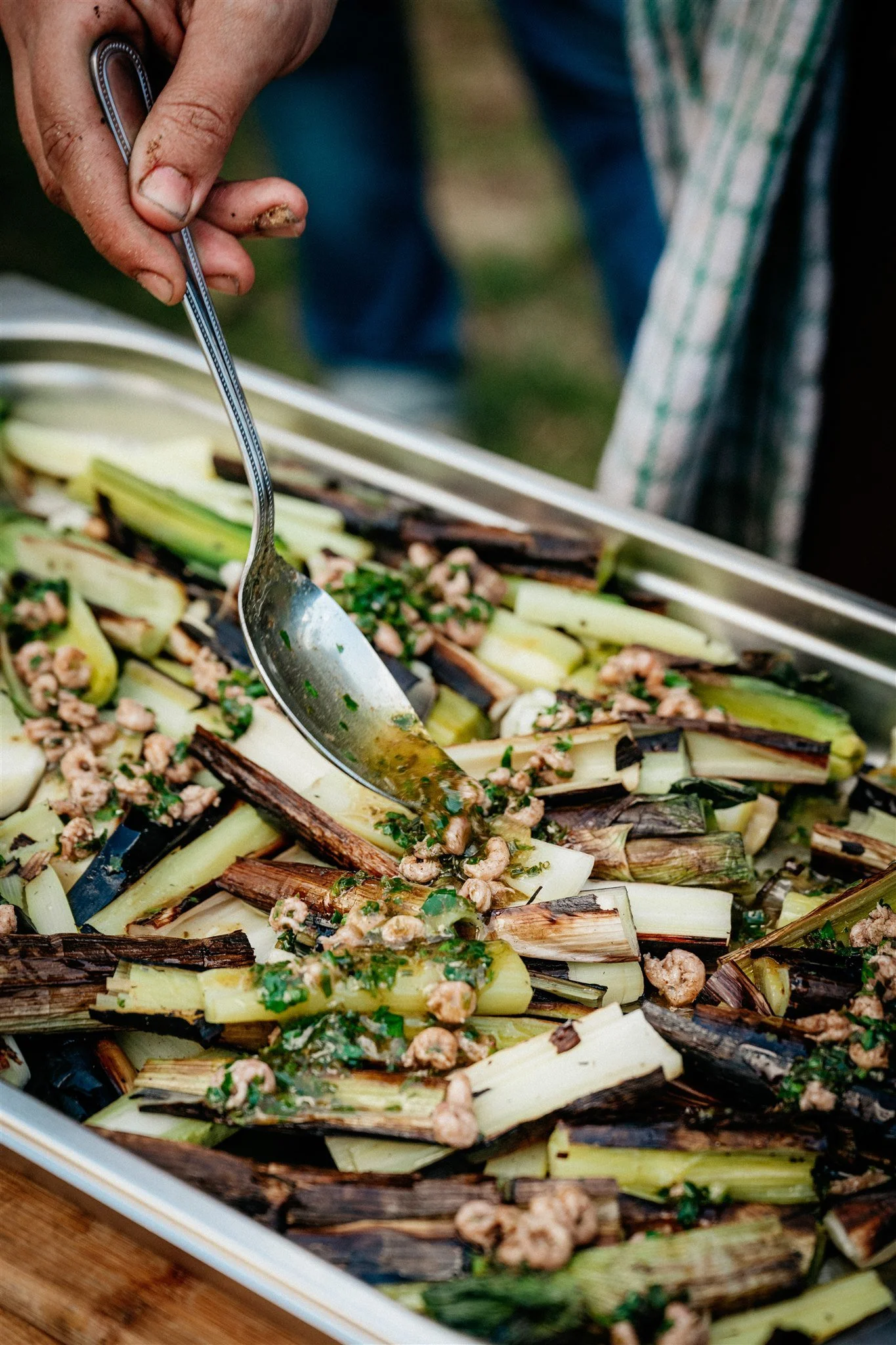 A close-up of someone holding a fork and tending to a dish of grilled vegetables, including eggplant and chopped herbs.