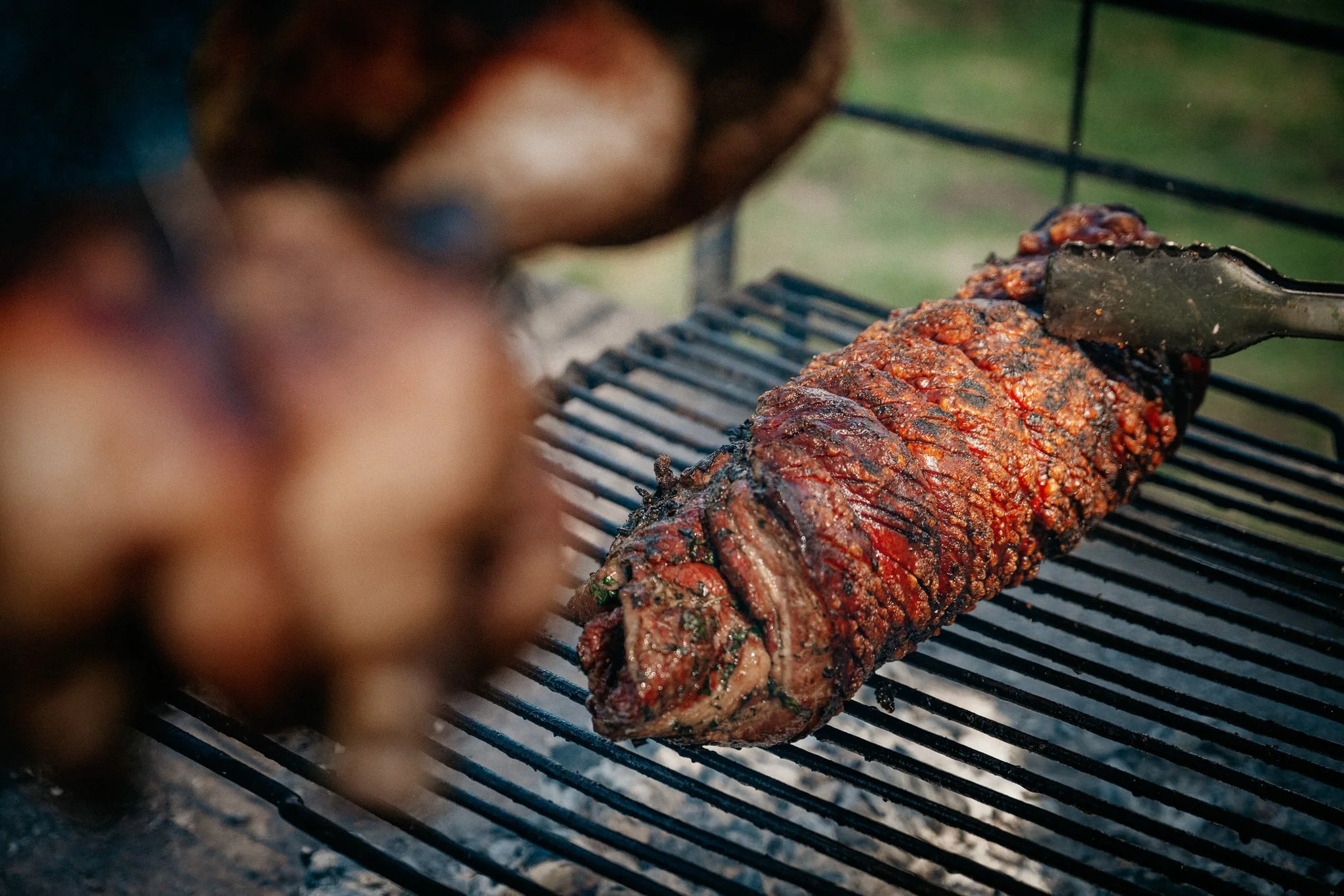 A barbecue grill with a large piece of seasoned meat, possibly a beef roast, cooking on the grill with visible grill lines and a slightly charred surface.