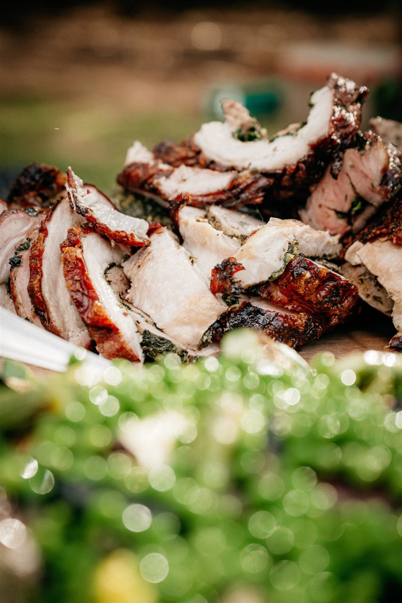 Close-up of sliced grilled pork with herbs and spices, placed on a plate, with a blurred green and yellow background.
