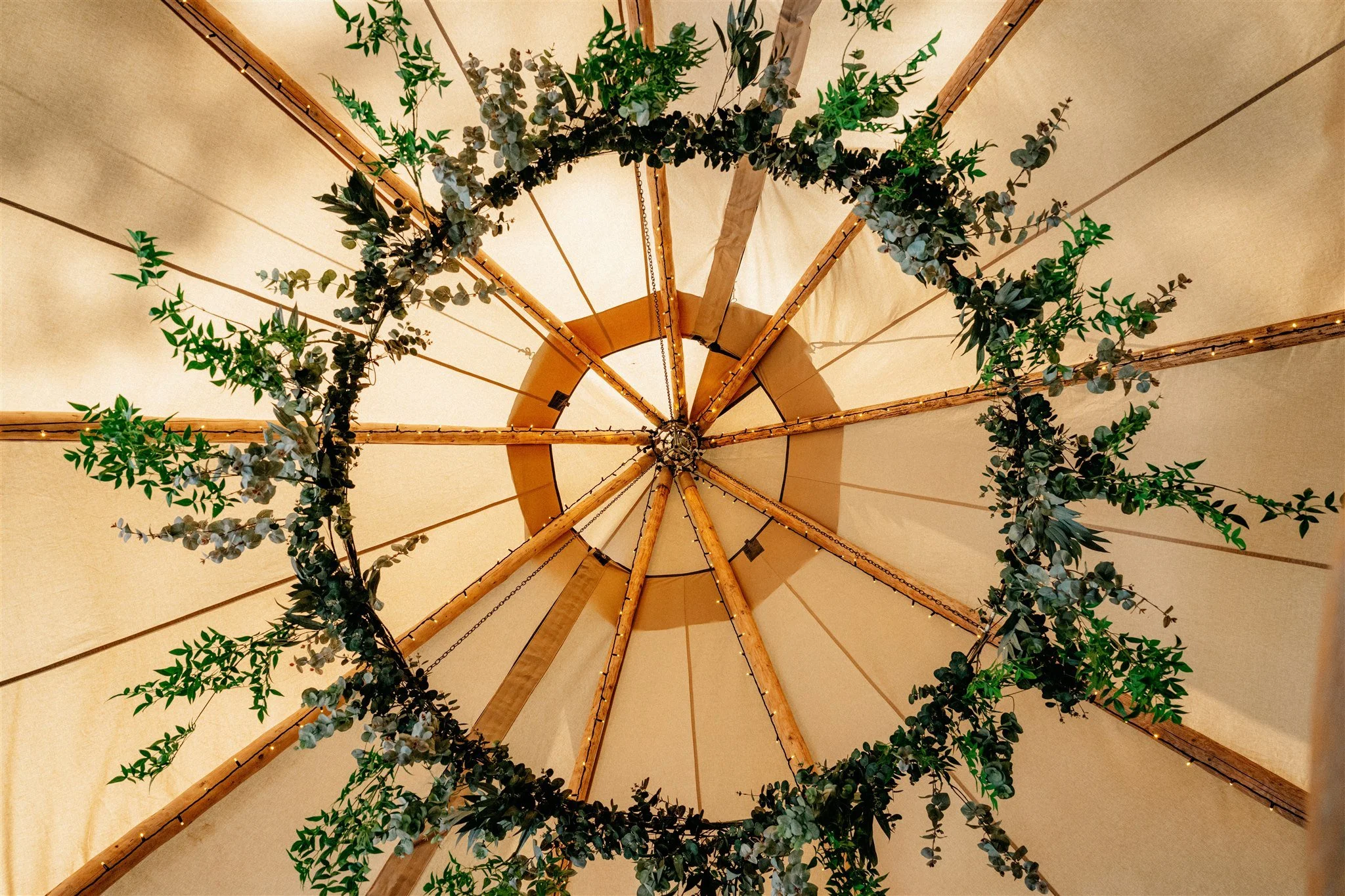 Interior view of a ceiling with wooden beams and a large light fixture decorated with green foliage and small string lights.