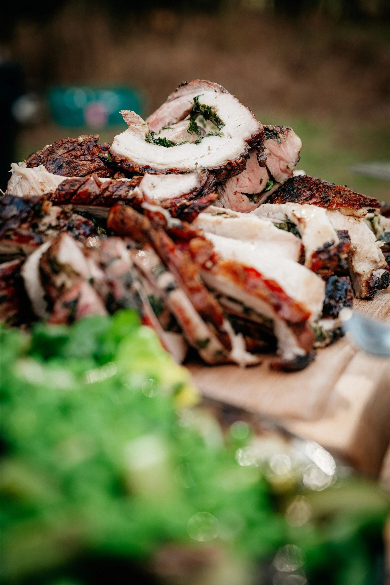 Close-up of cooked pork tenderloin stuffed with herbs, sliced to reveal the stuffing, on a platter with some green garnish.