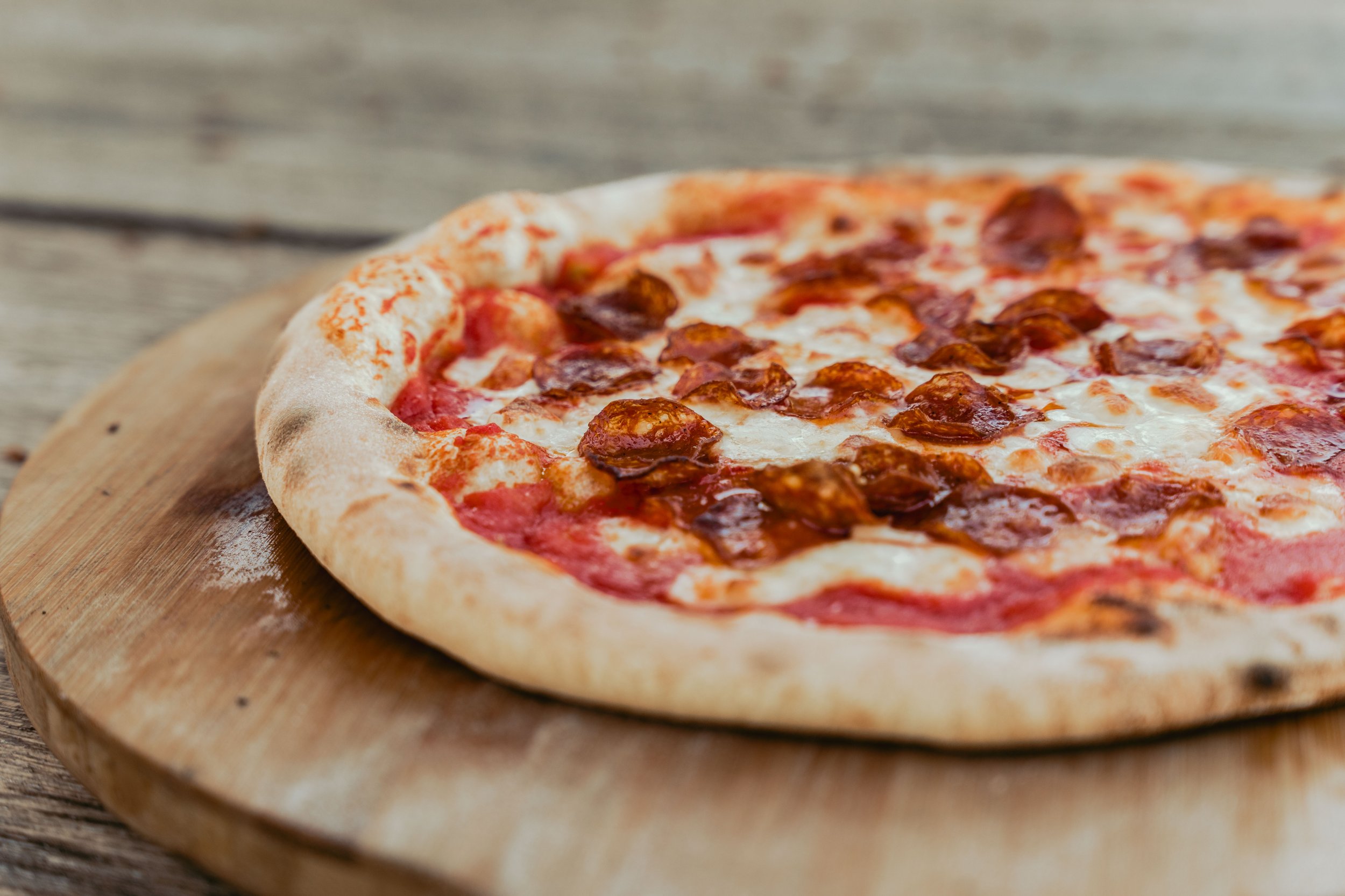 A pepperoni pizza with melted cheese on a wooden pizza peel.