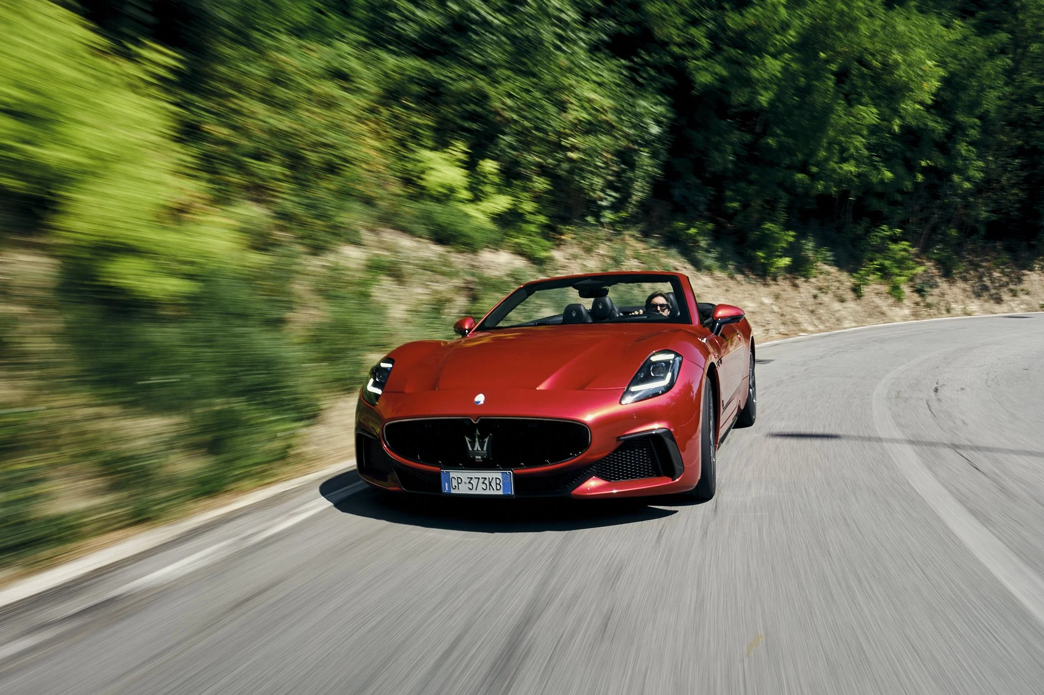 A red sports car driving on a winding road through a green forest.