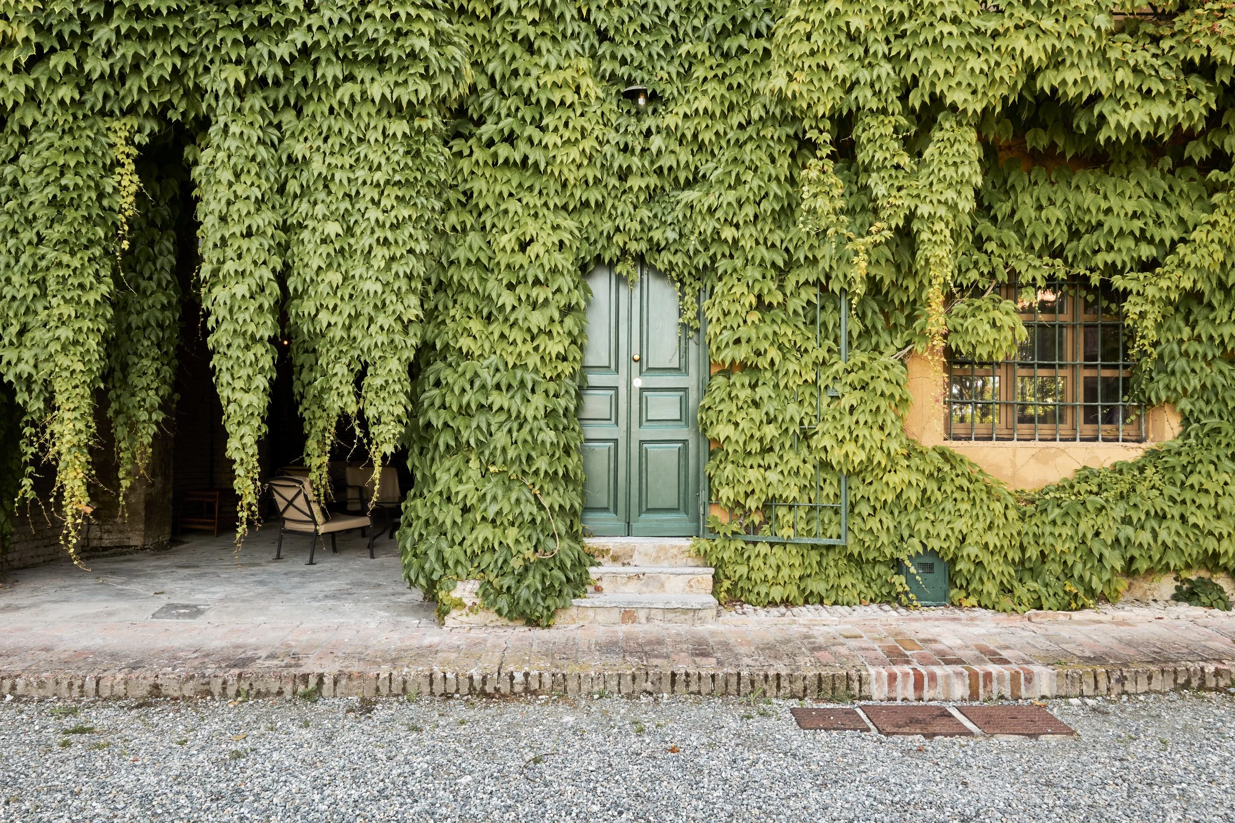 A building covered in green ivy with a green double door and a window with bars on the right side.