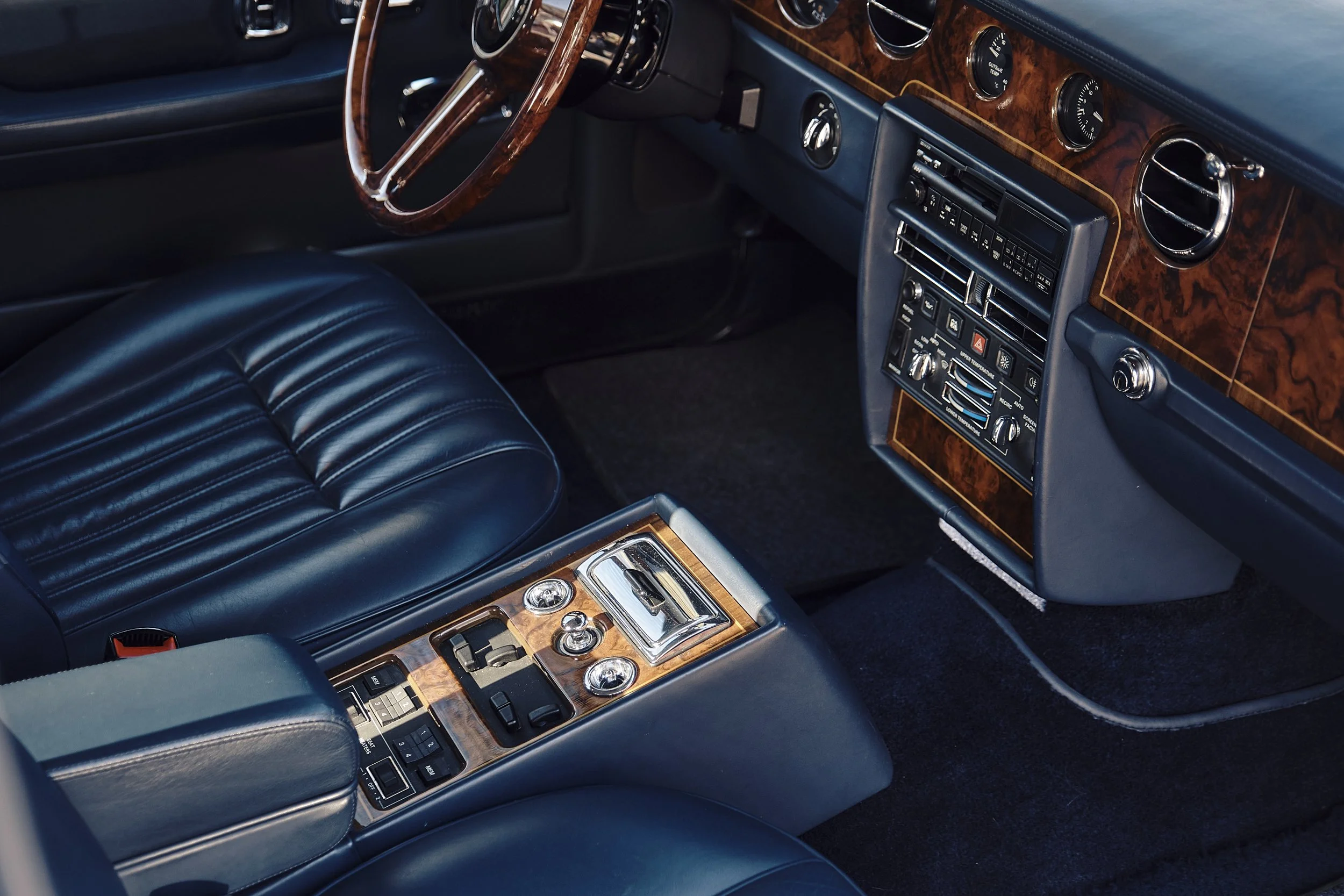 Interior of a vintage car featuring a wood grain dashboard, black leather seats, and a wooden steering wheel.