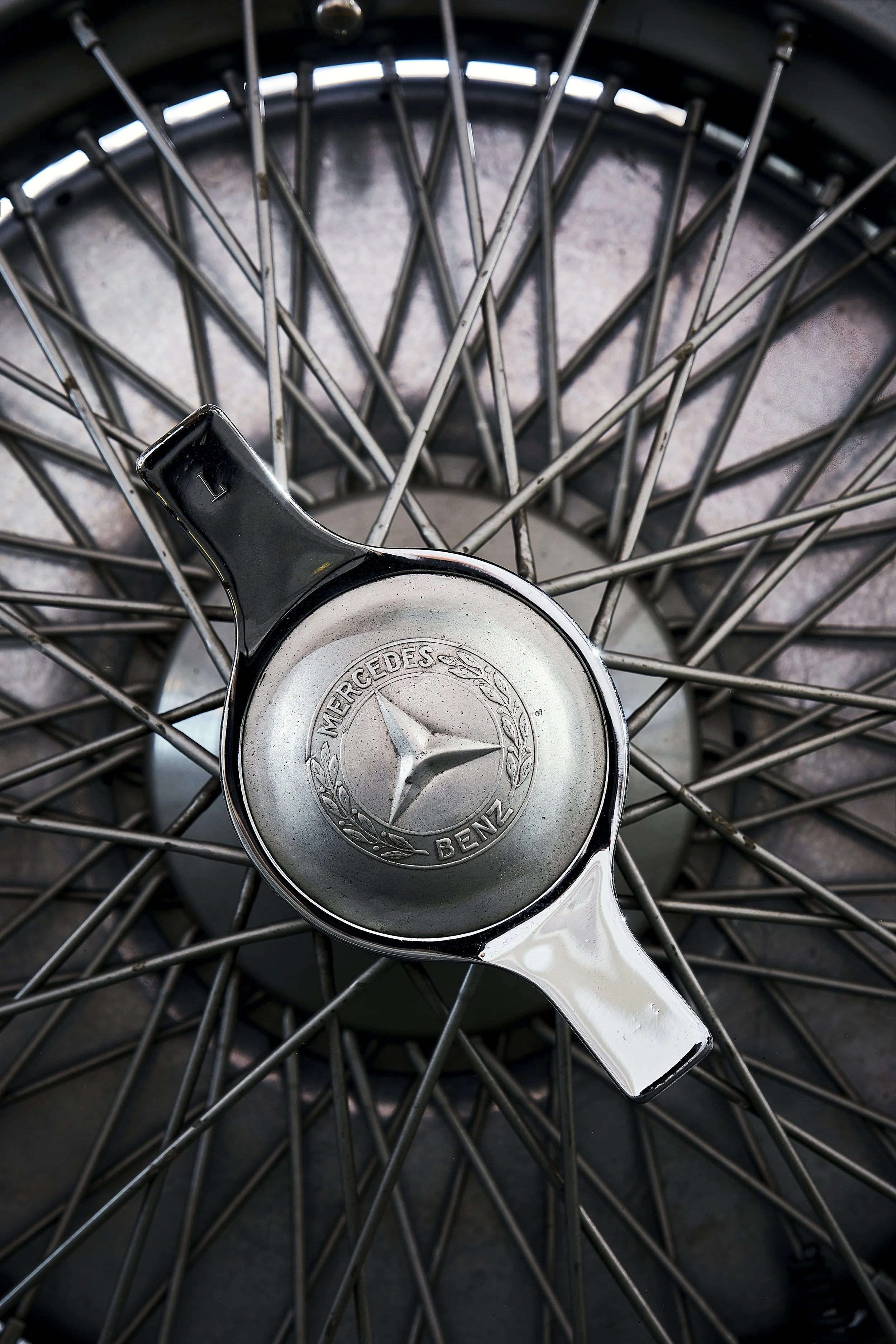 Close-up of a Mercedes-Benz wheel hubcap with spoked rim visible in the background.