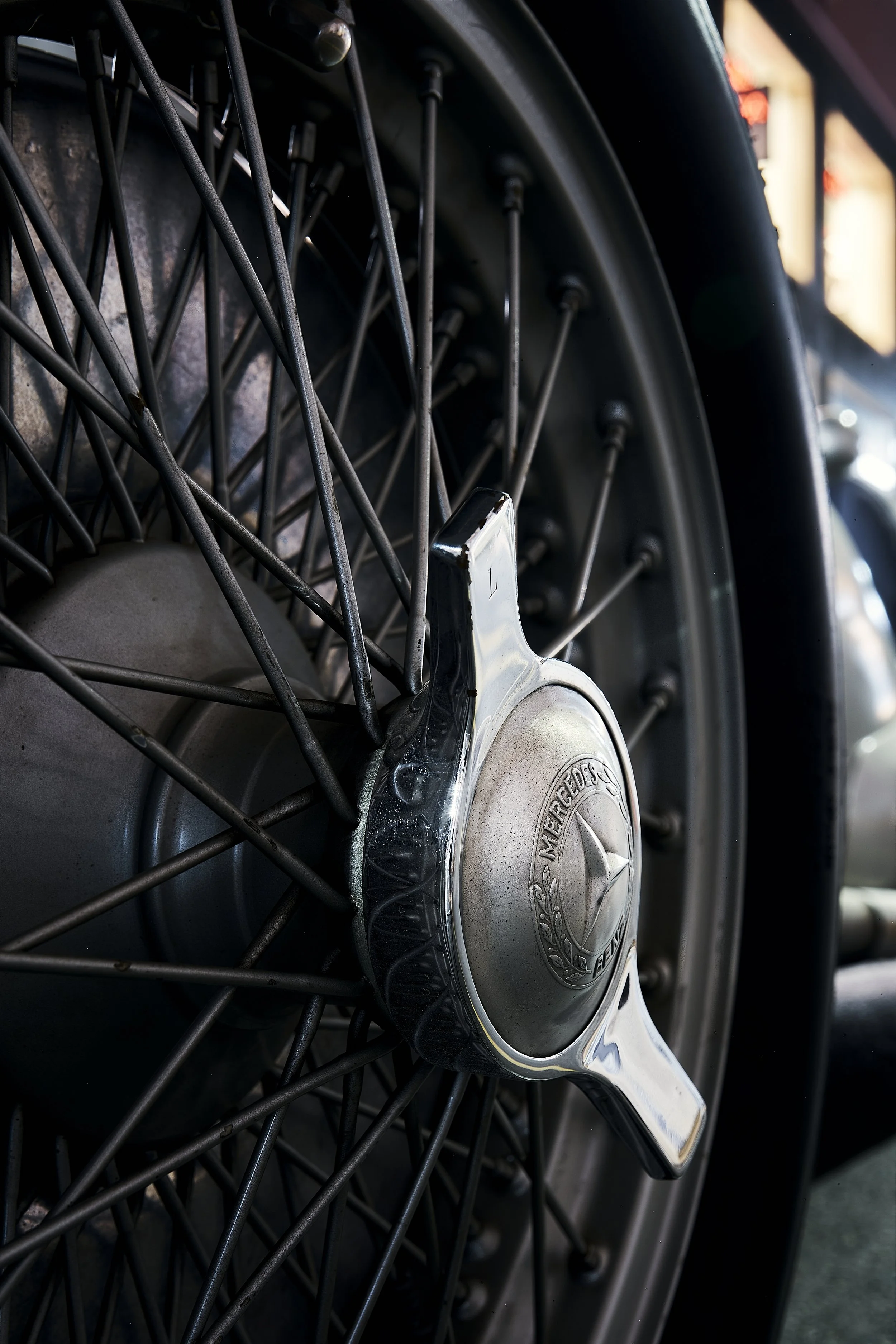 Close-up of a vintage Mercedes-Benz car wheel with a star emblem on the hubcap and wire spokes.
