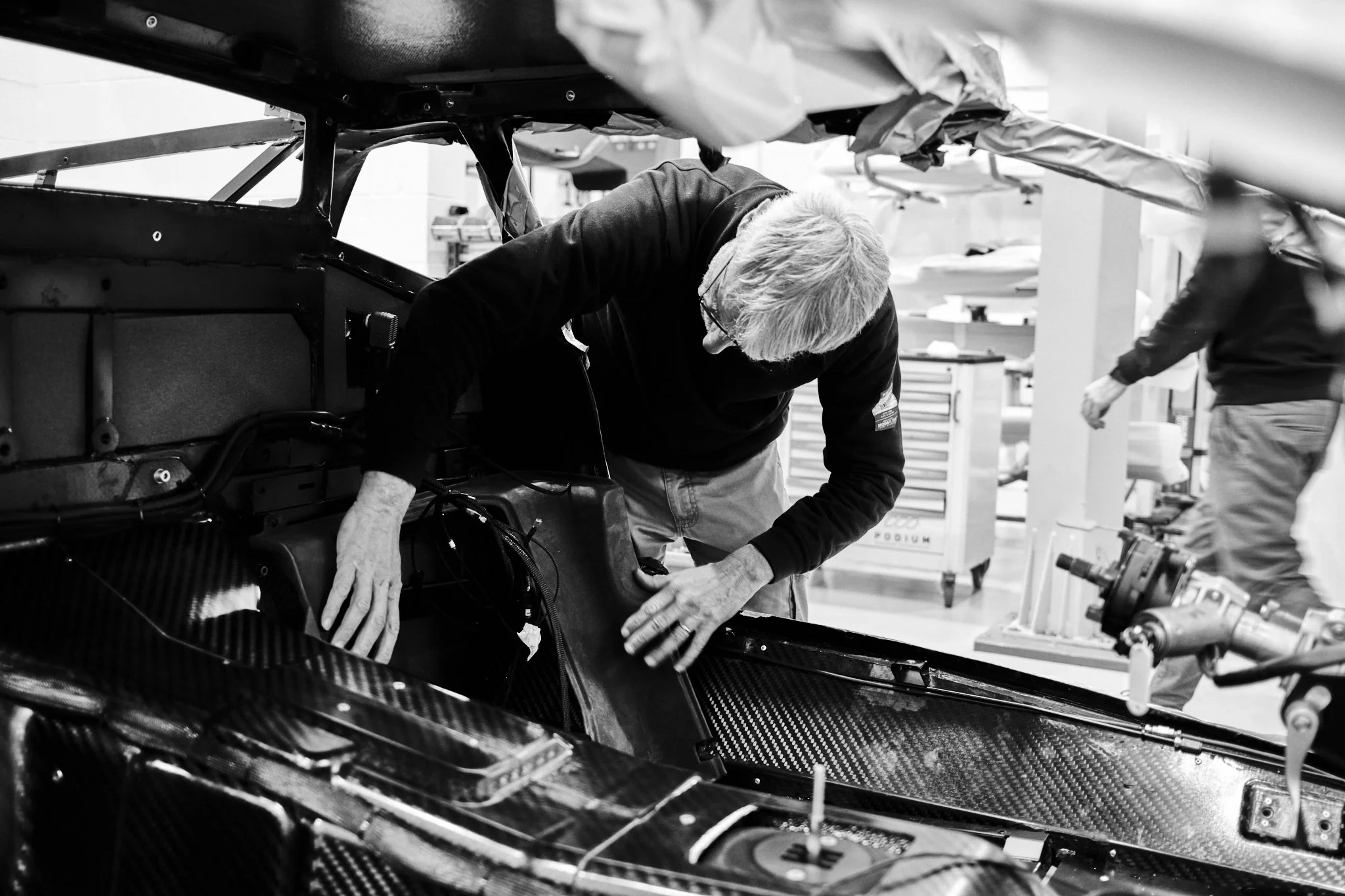 A person inspecting or working on the inside of a race car chassis in a workshop or garage.