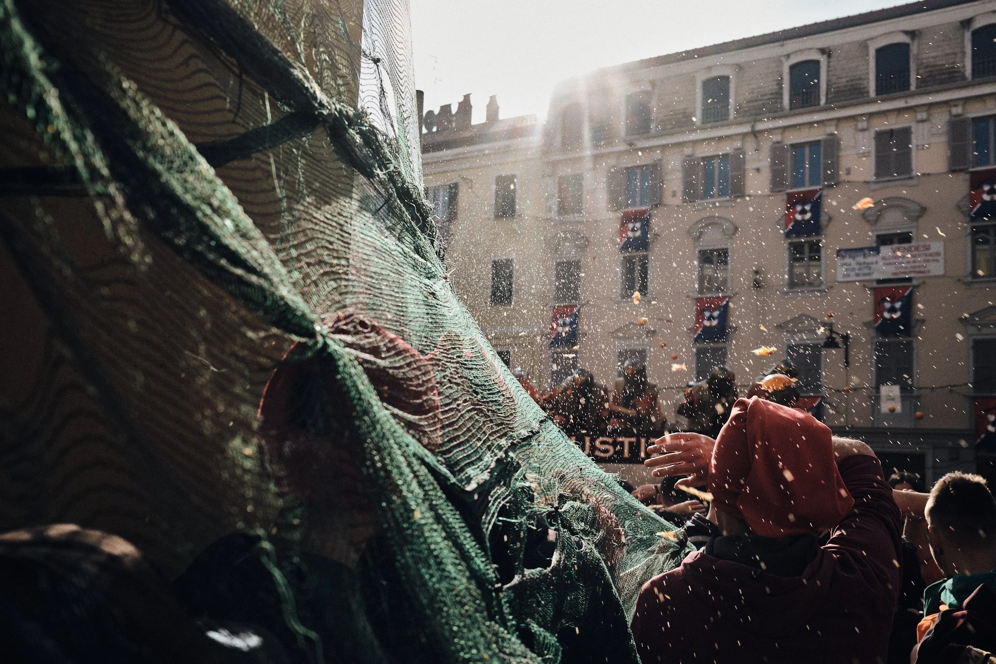 People celebrating in a street parade with a large dragon puppet, sunlight shining down, and US flags hanging on buildings.