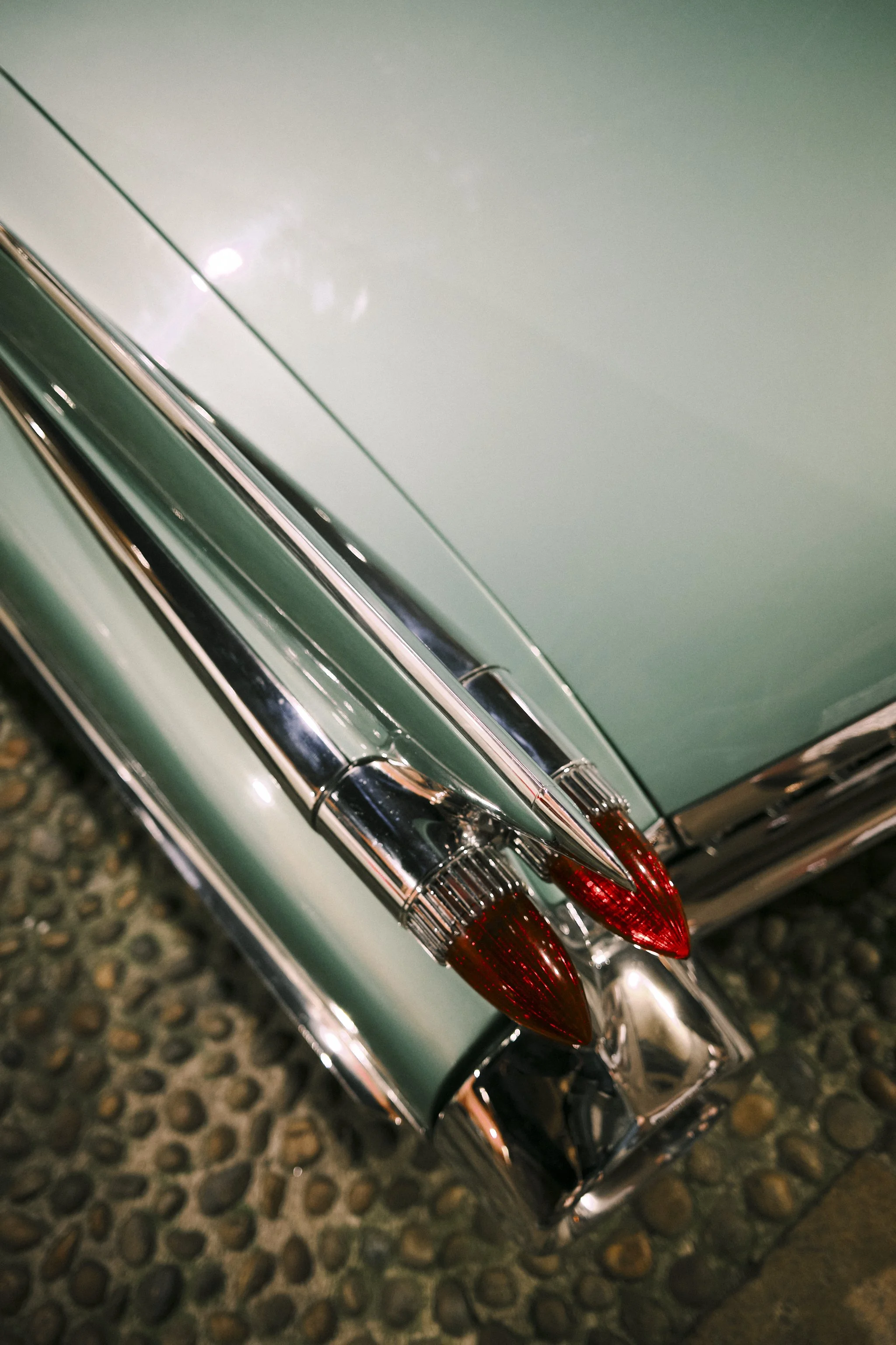 Close-up of the tail fins and taillights of a vintage pastel green car on a cobblestone surface.