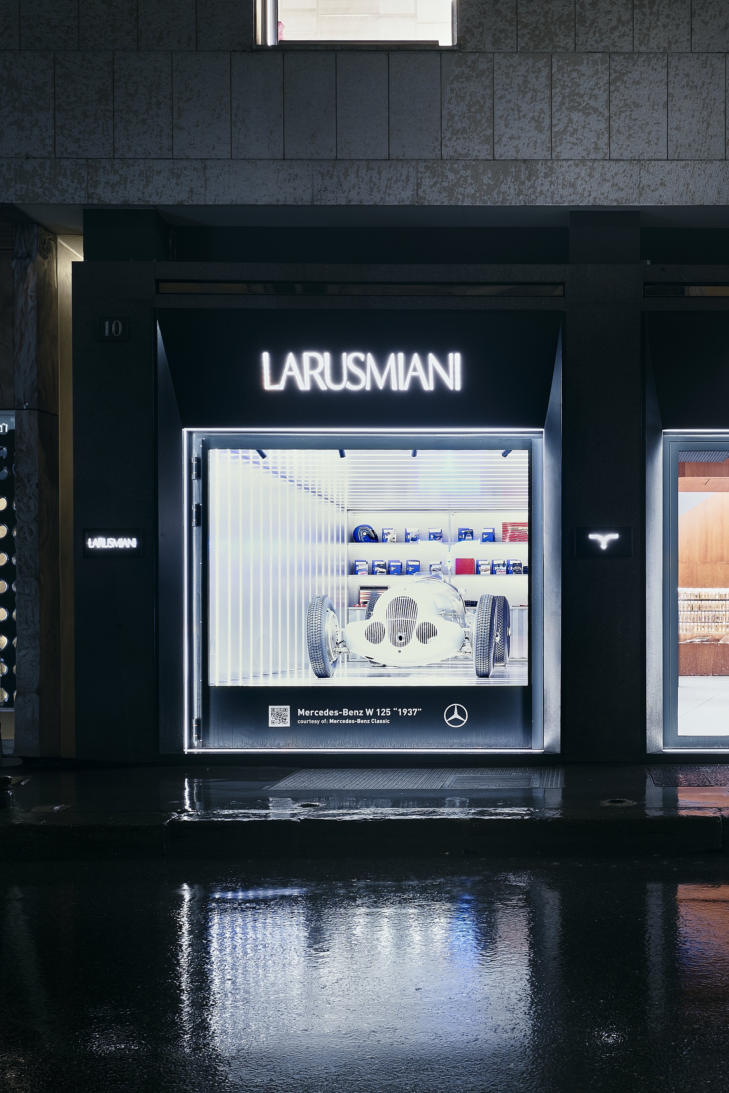 Display window for La Rusmiani featuring a vintage Mercedes-Benz W 125 racing car from 1937, with shelves of model cars and memorabilia visible inside.