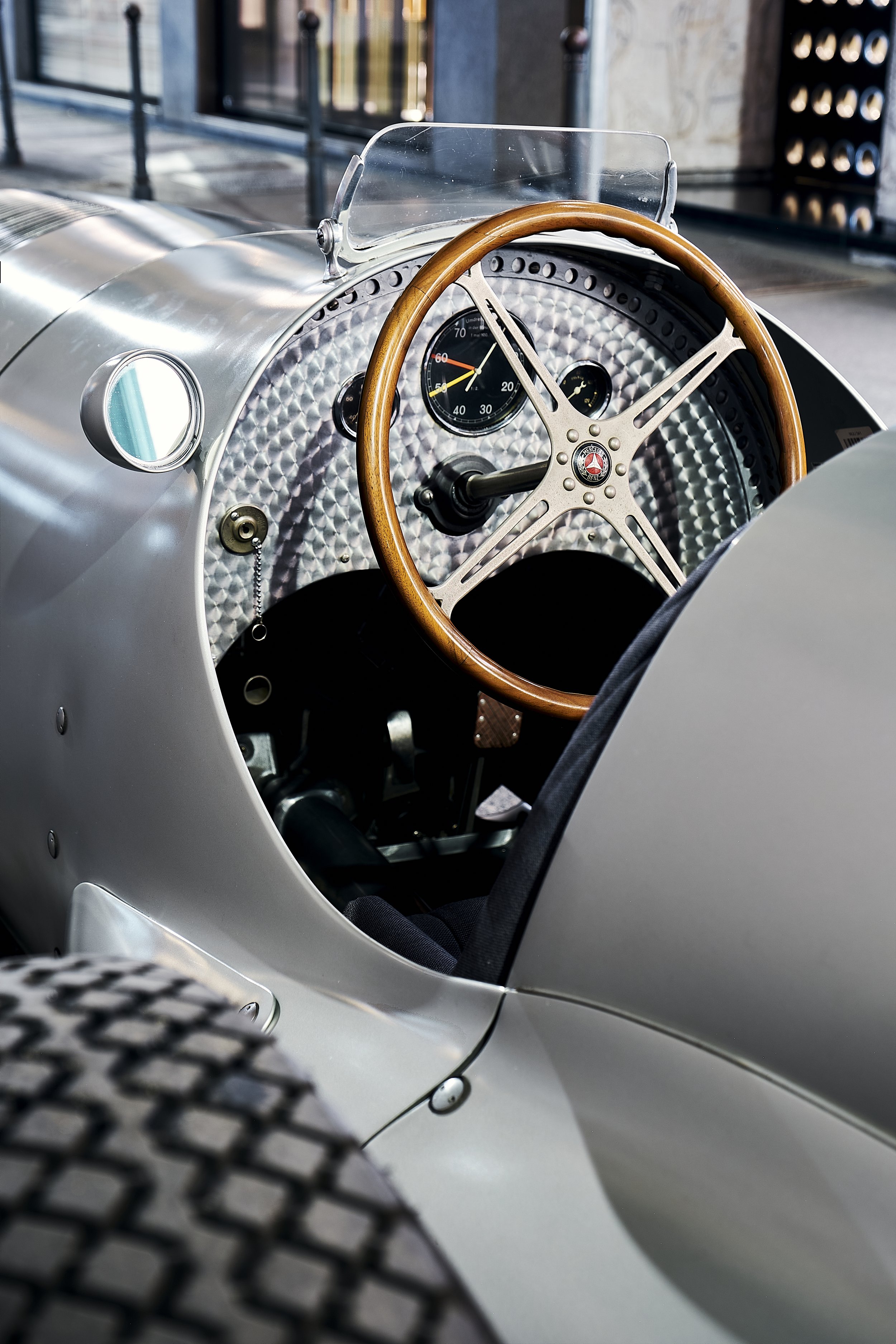 Close-up of the dashboard and steering wheel of a vintage racing car with a wooden steering wheel and modern gauges, parked outdoors.