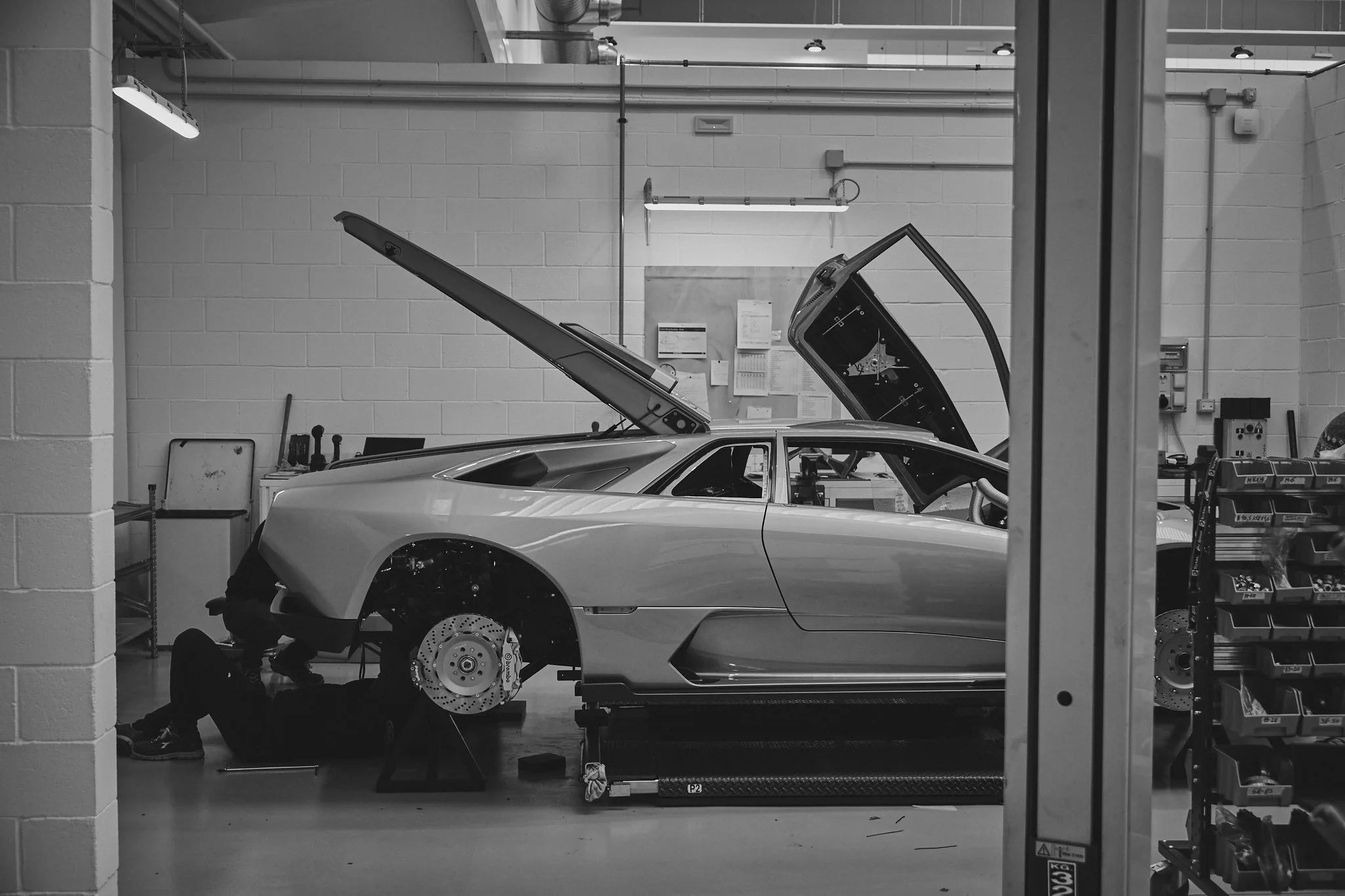 Inside a workshop with a sports car being assembled, with its wheels and some parts missing and tools nearby.