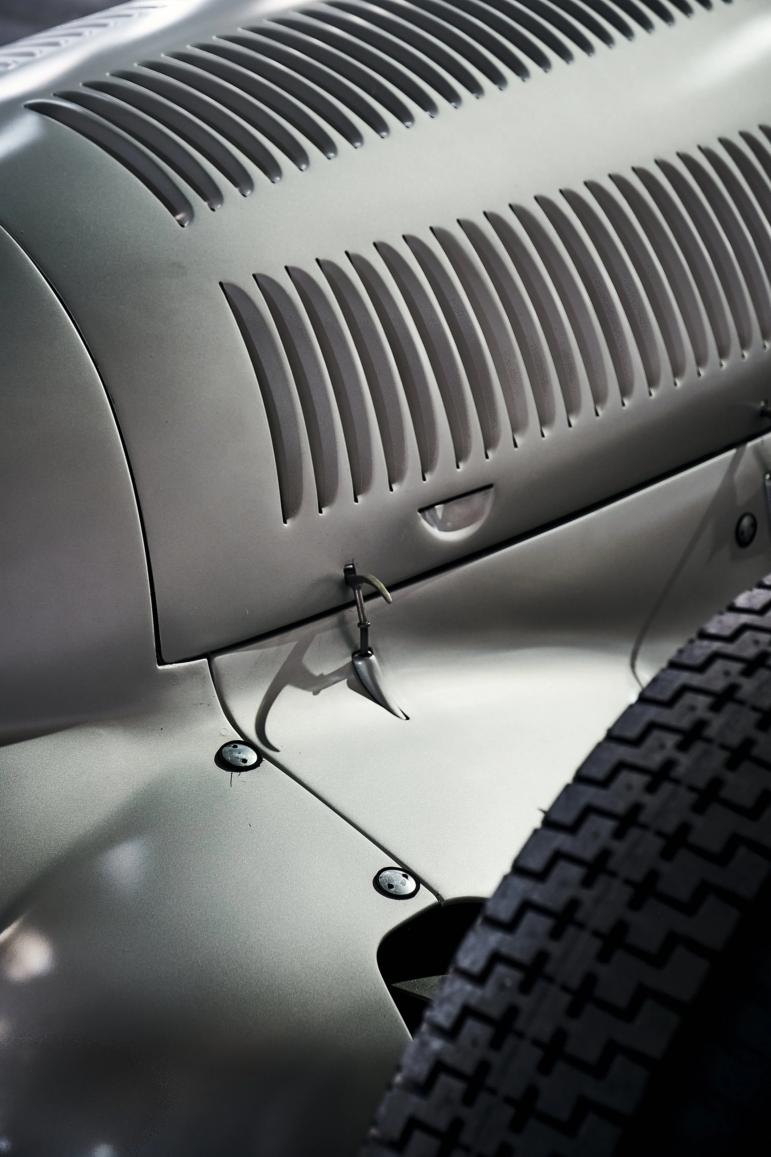 Close-up of the side panel and wheel of a vintage car, showing metal vents, rivets, and part of a textured tire.