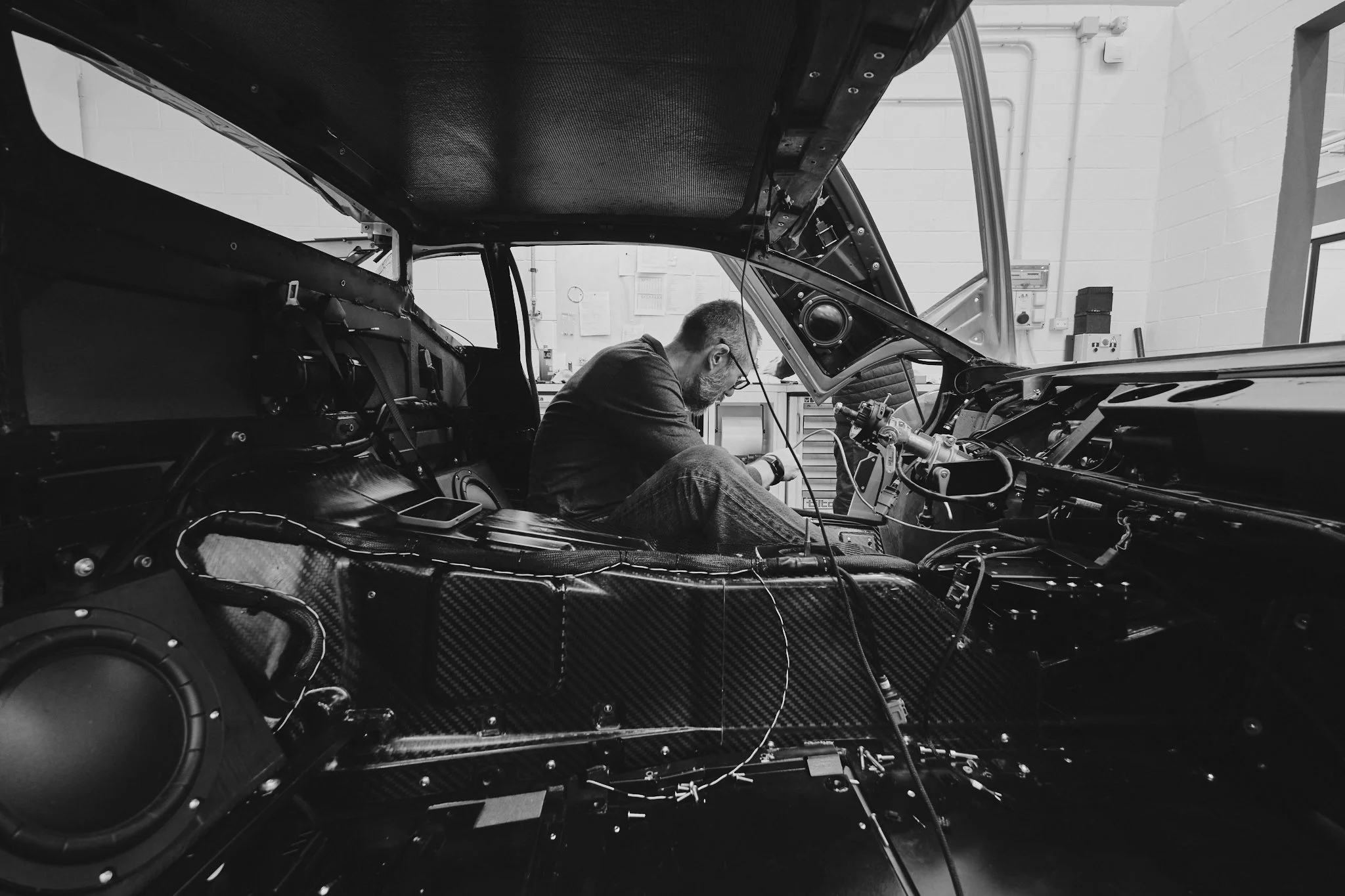 A person working inside a racing car, focused on the dashboard and wiring, in a garage setting.
