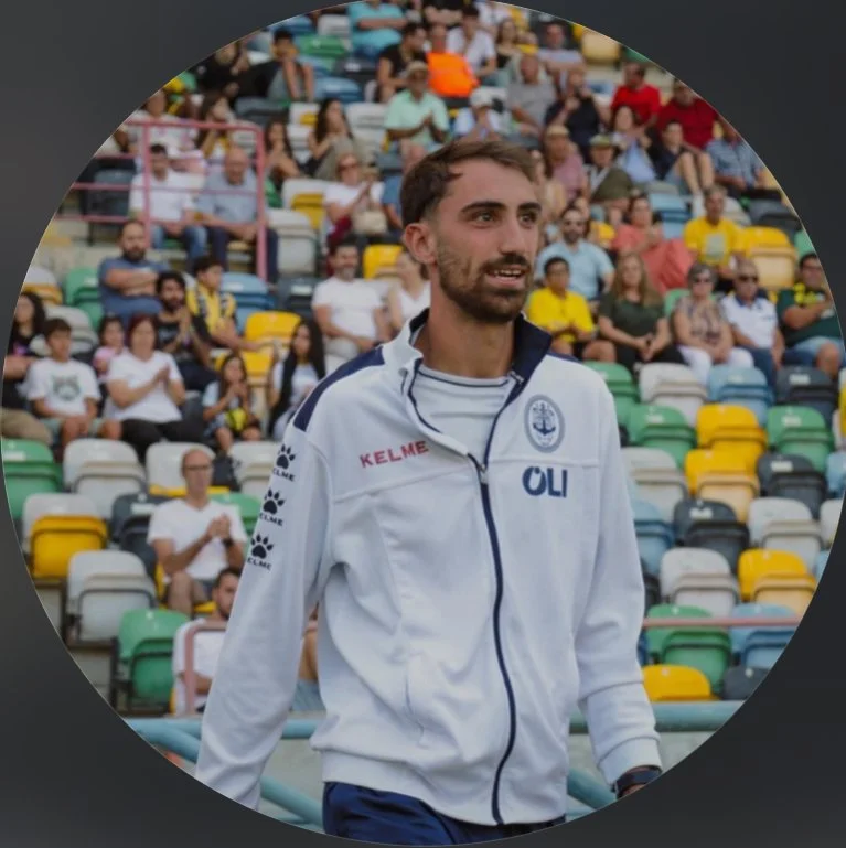 A man in a white sports jacket walking on a stadium field with a crowd of spectators in the background.