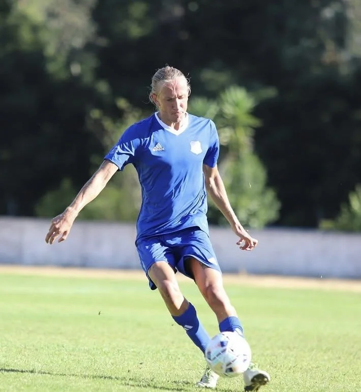 Female soccer player in blue uniform kicking a soccer ball on a field.
