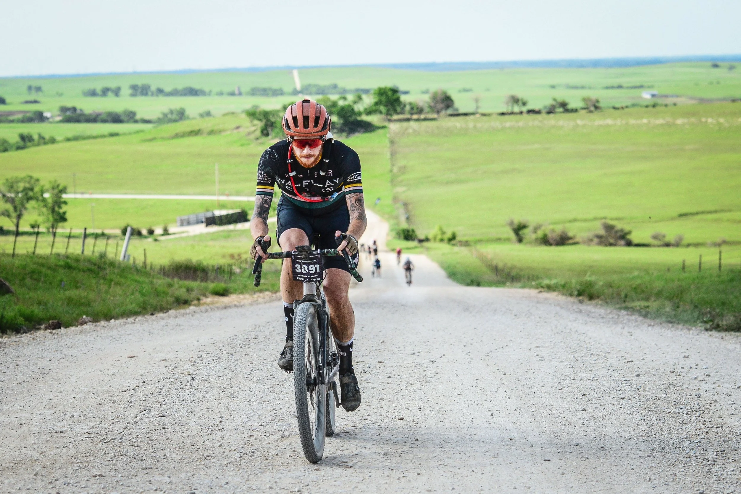 A man riding a mountain bike on a gravel road through scenic green countryside, wearing a red helmet and black cycling gear.