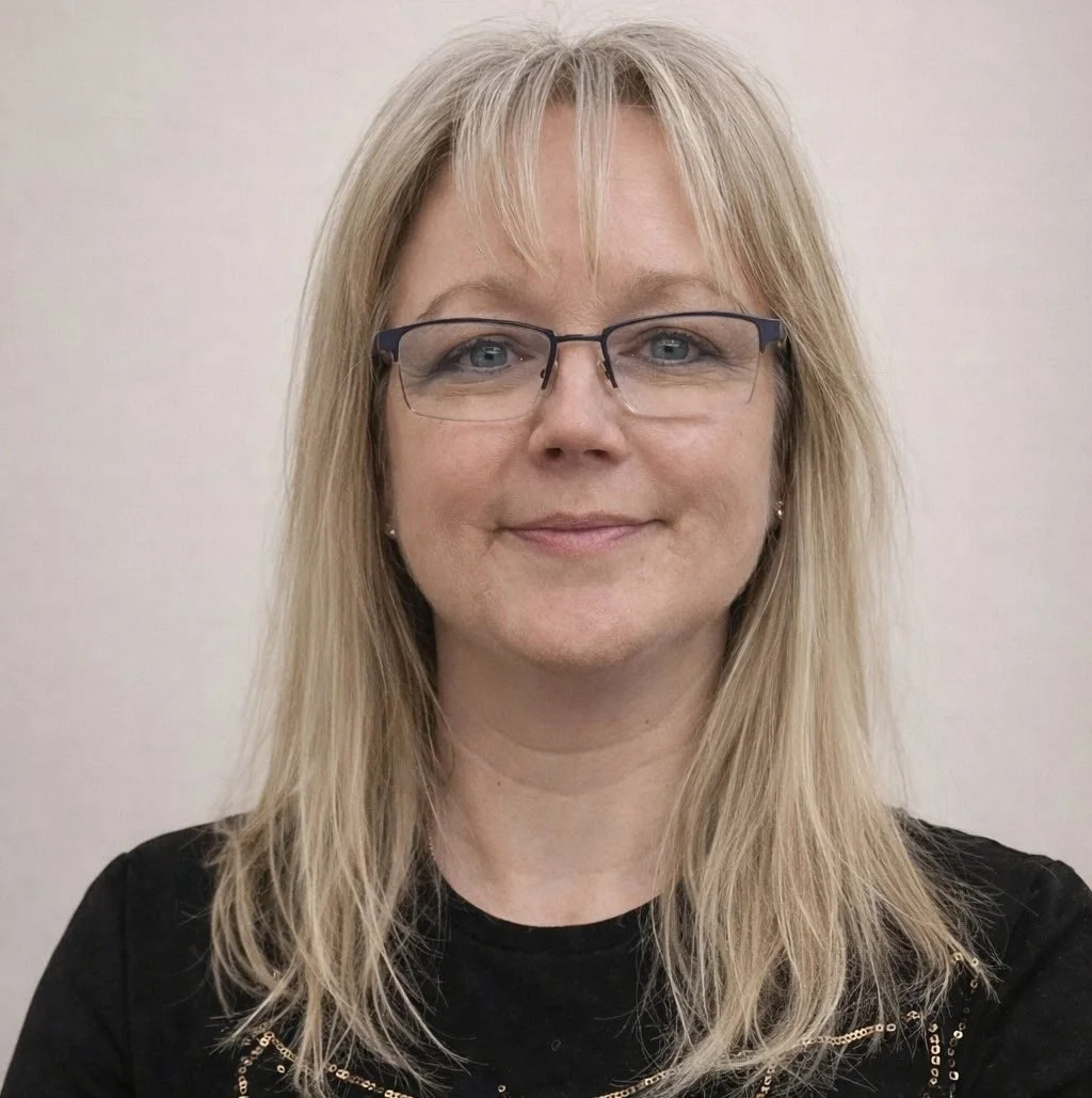 A woman with blonde hair, glasses, and earrings, smiling at the camera, wearing a black top with gold accents.