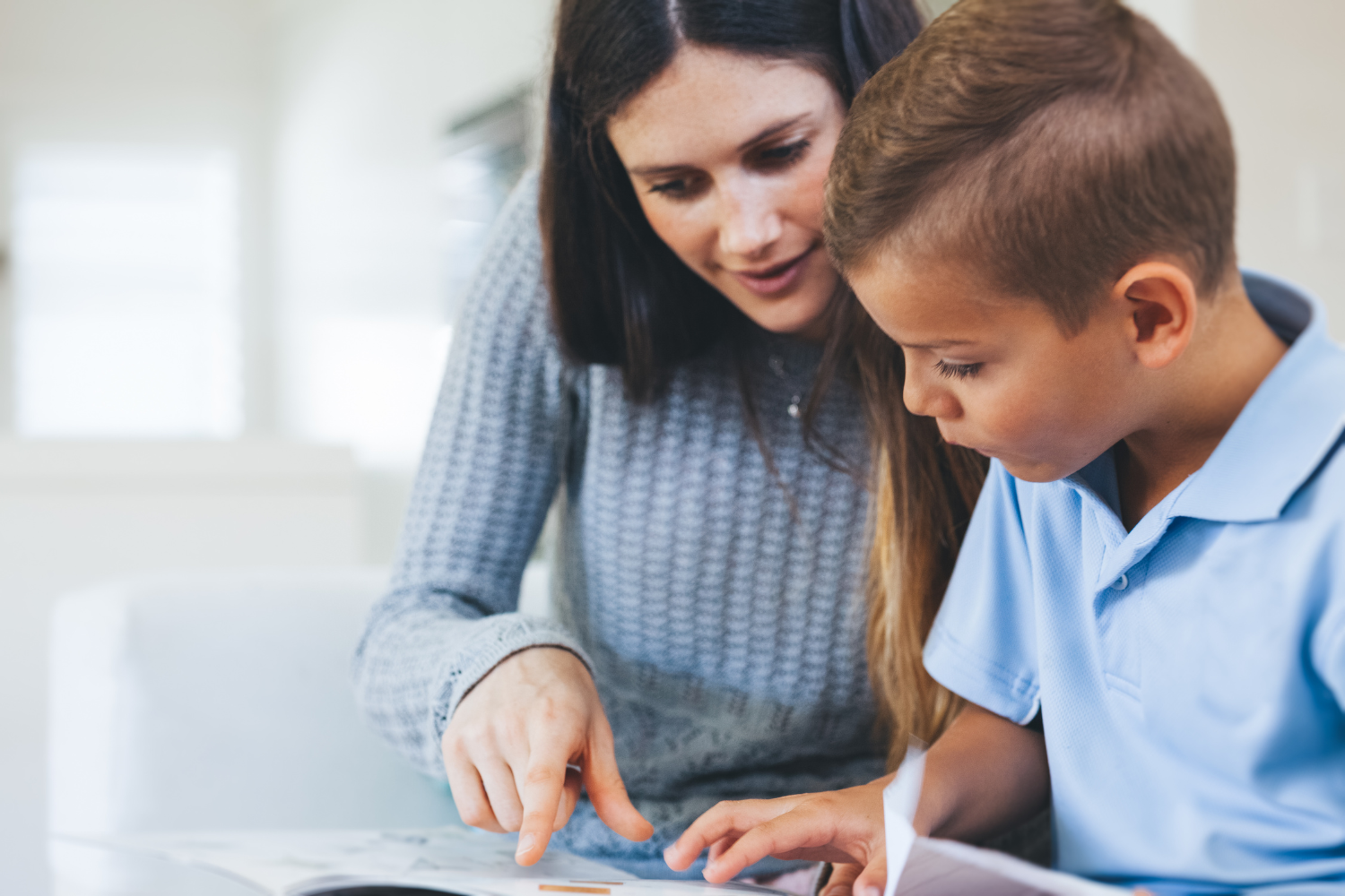 A woman and a young boy look at papers on a table, with the woman pointing at something.