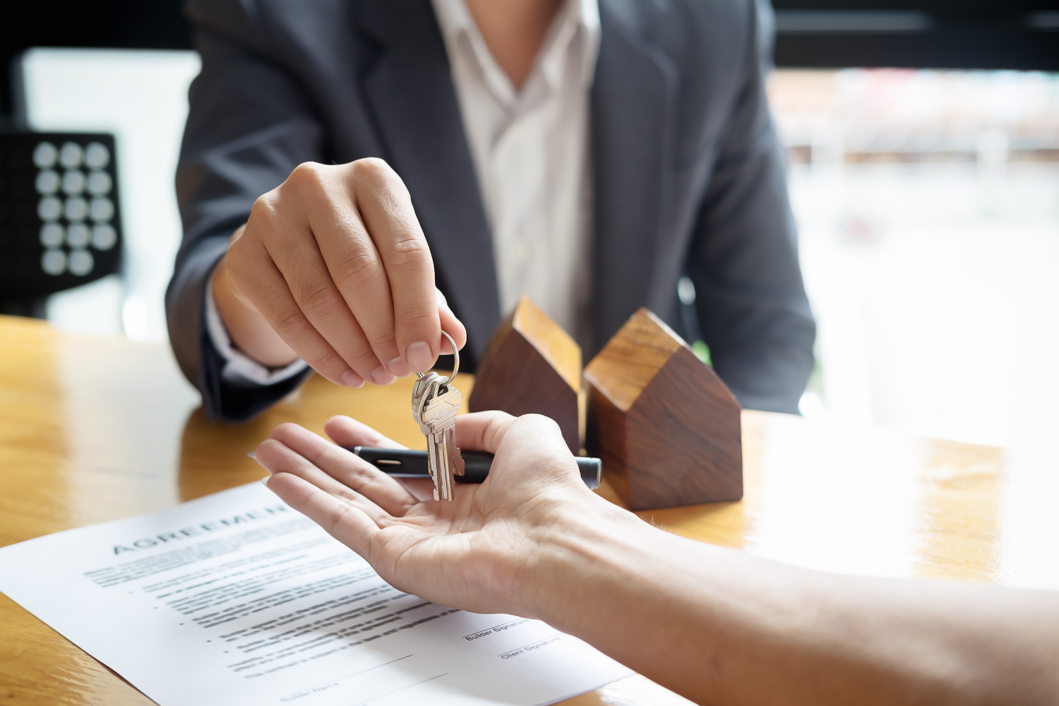 Person in a suit handing over keys to another person in a bright room during a real estate transaction or signing agreement.