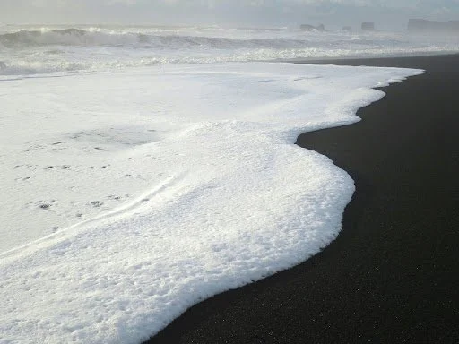 Ocean waves washing onto a black sand beach.