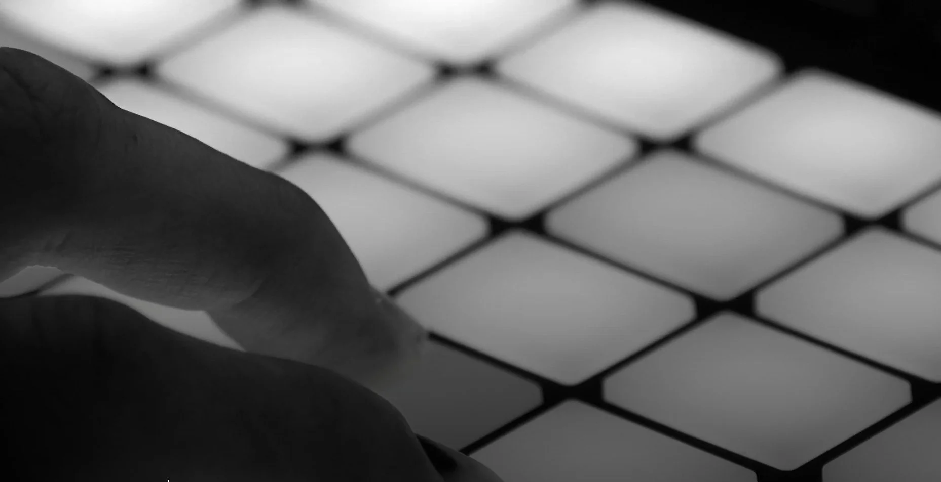 Close-up black and white photo of a finger touching a surface with a grid-like pattern.