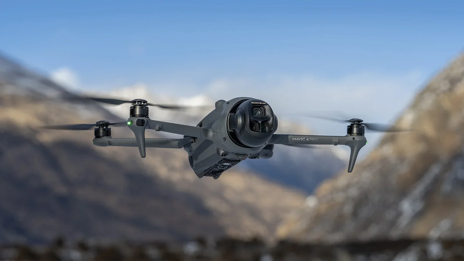 DJI Mavic 4 Pro drone flying over a rugged mountain landscape with snow-covered peaks.