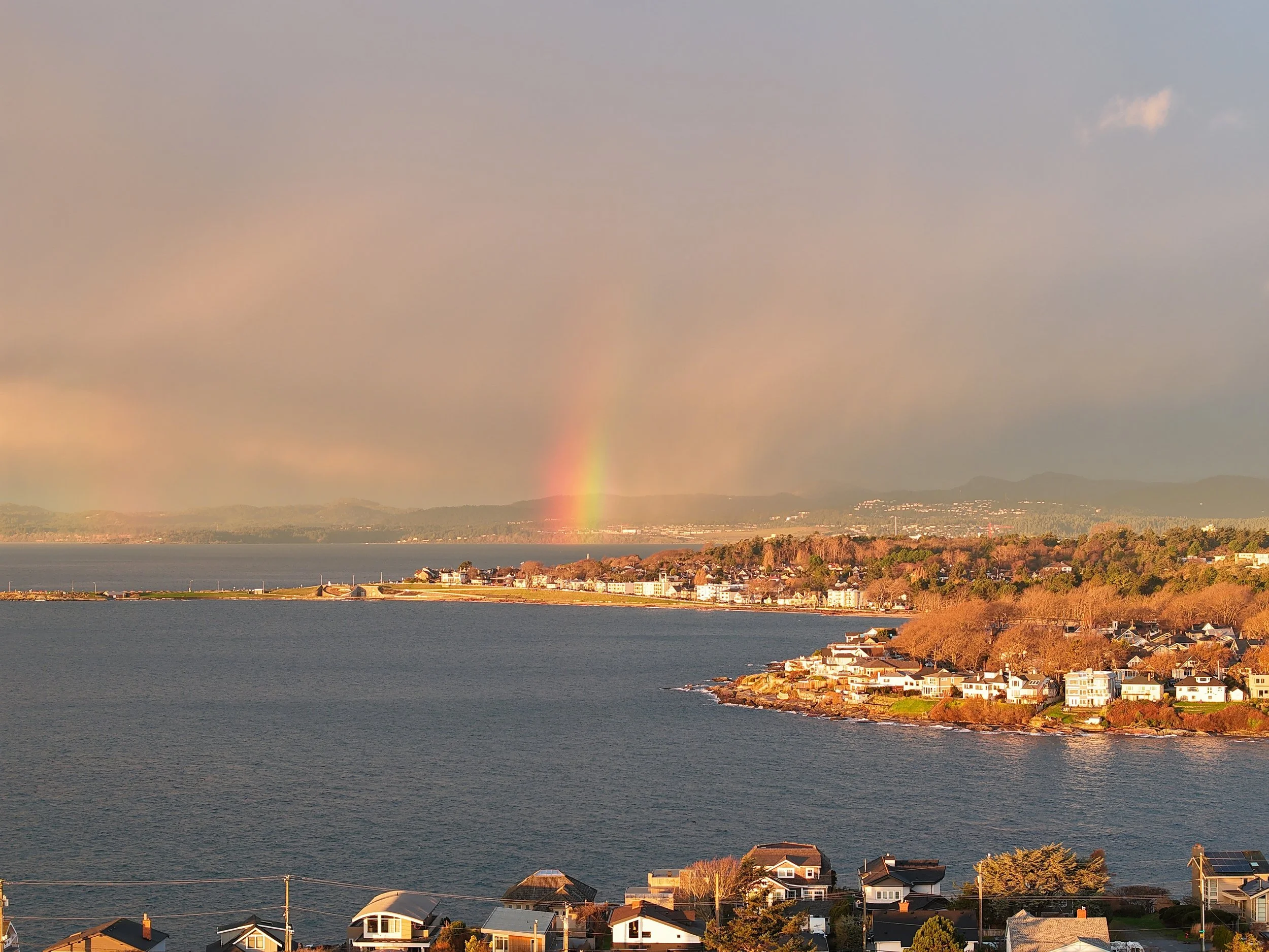 A brief rainbow appears through coastal mist after the rain, looking across Gonzales Bay toward downtown Victoria. Soft light and low cloud create a subtle, atmospheric moment that passed as quickly as it arrived.