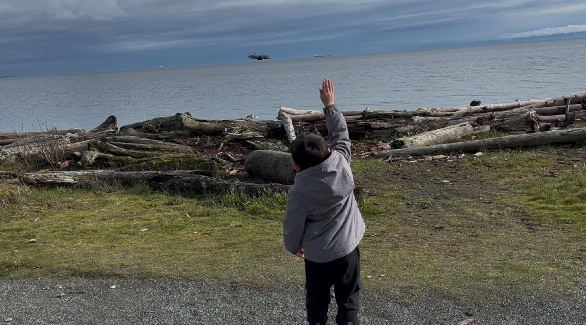 Child learning to fly a drone on a beach with DJI Neo 2 hovering in front of him
