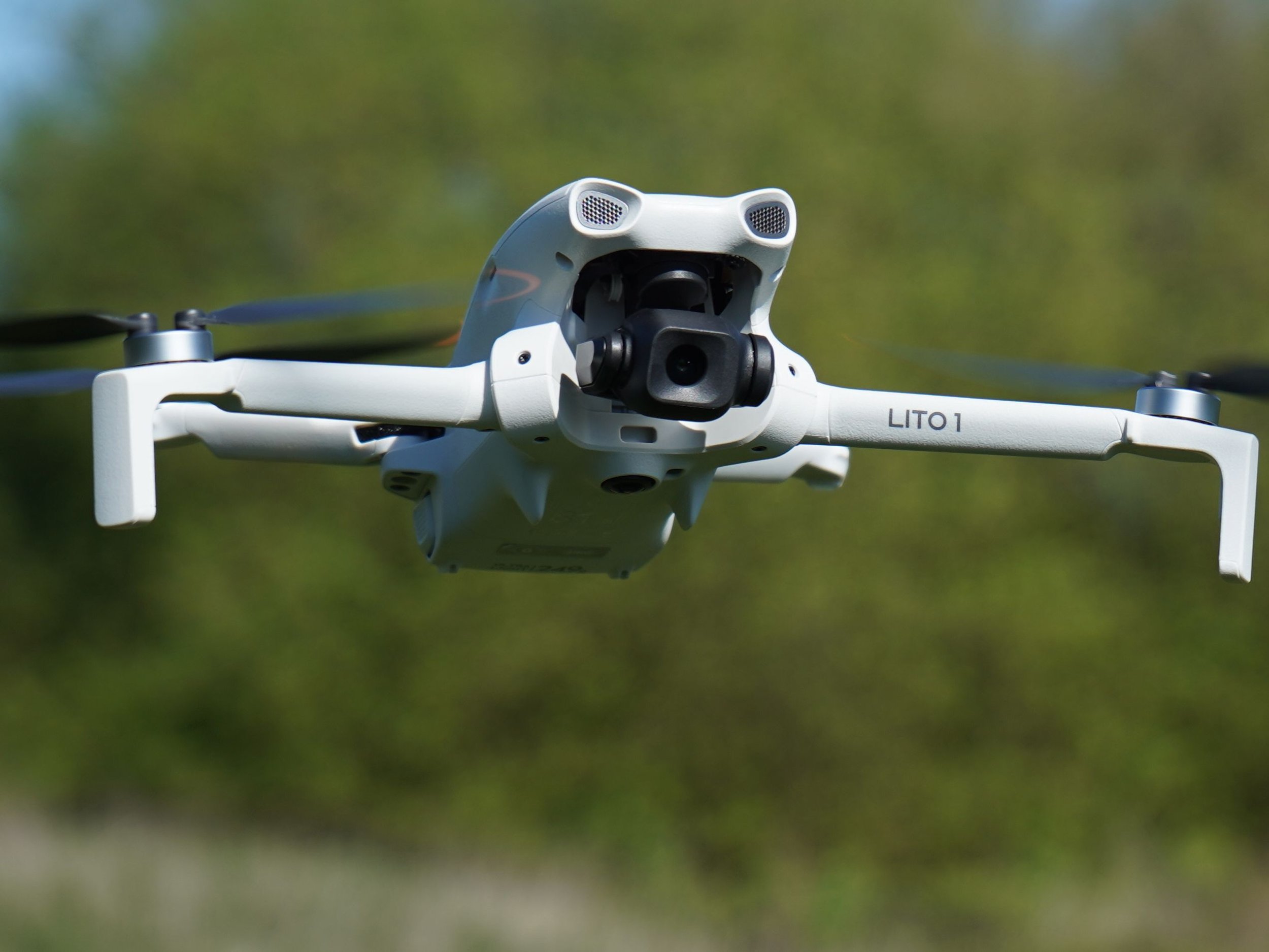 DJI Lito 1 drone flying outdoors against a blurred background of green trees and grass.