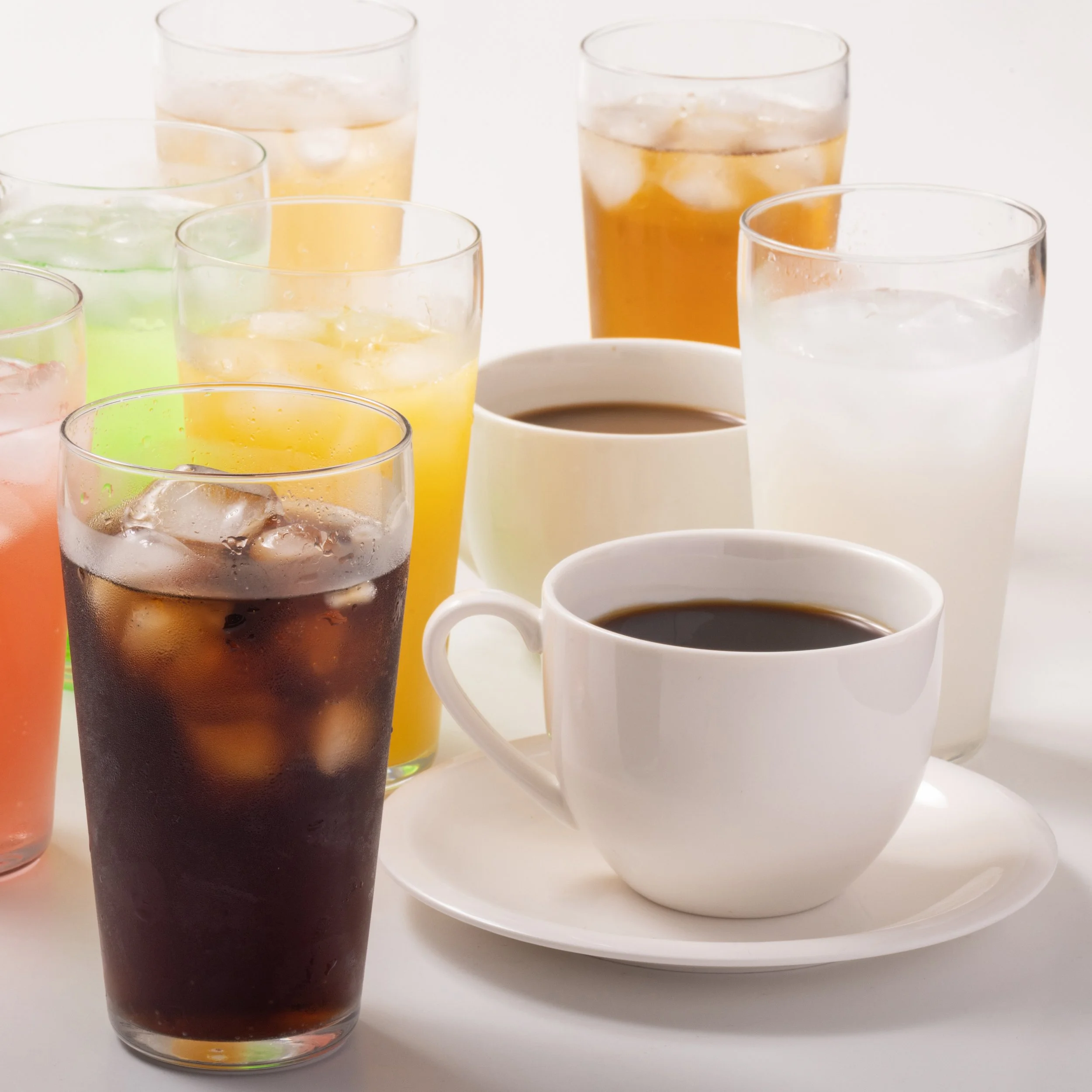 Various glasses of iced drinks and two cups of coffee on a white background.