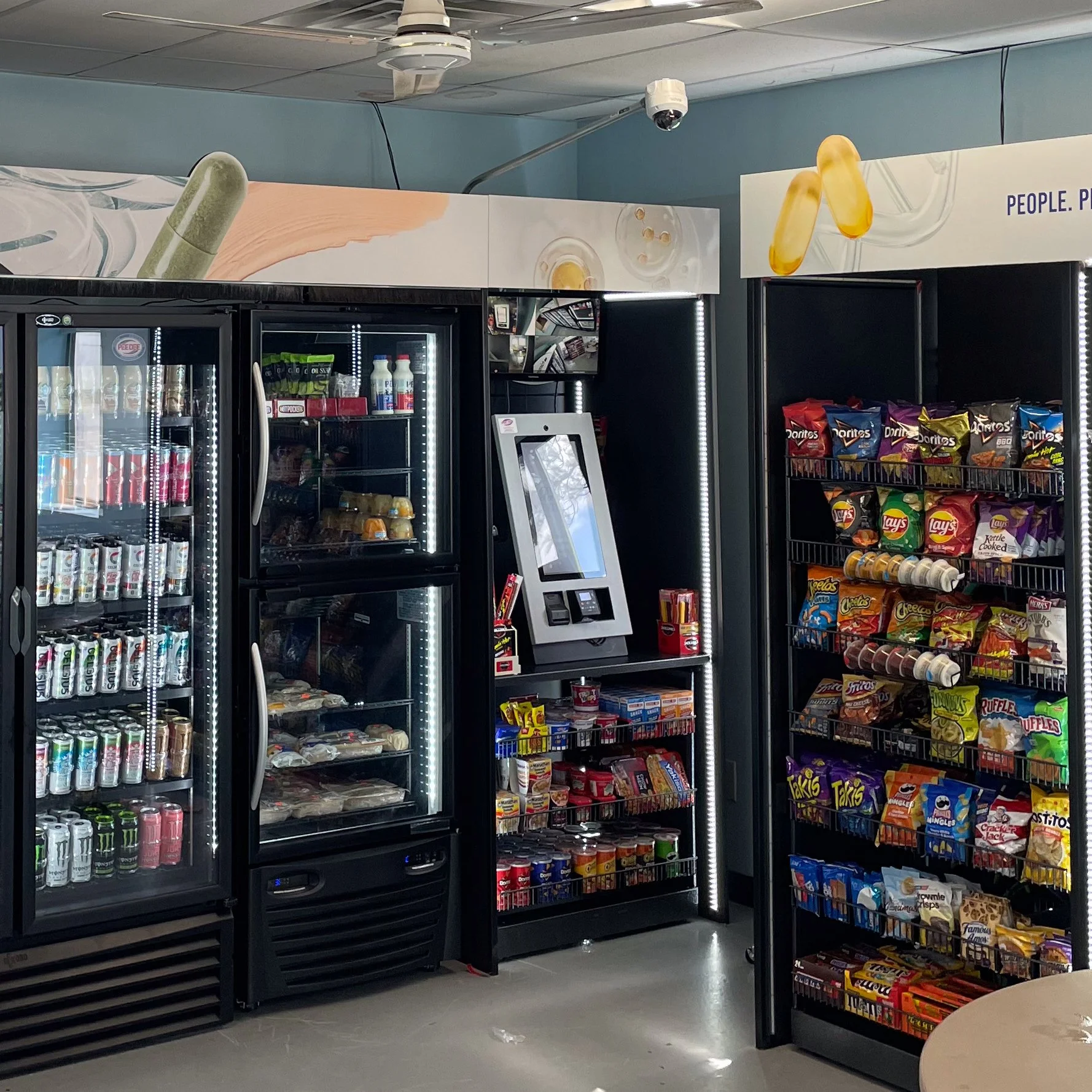Convenience store snack and beverage refrigerators with vending machine in the middle.