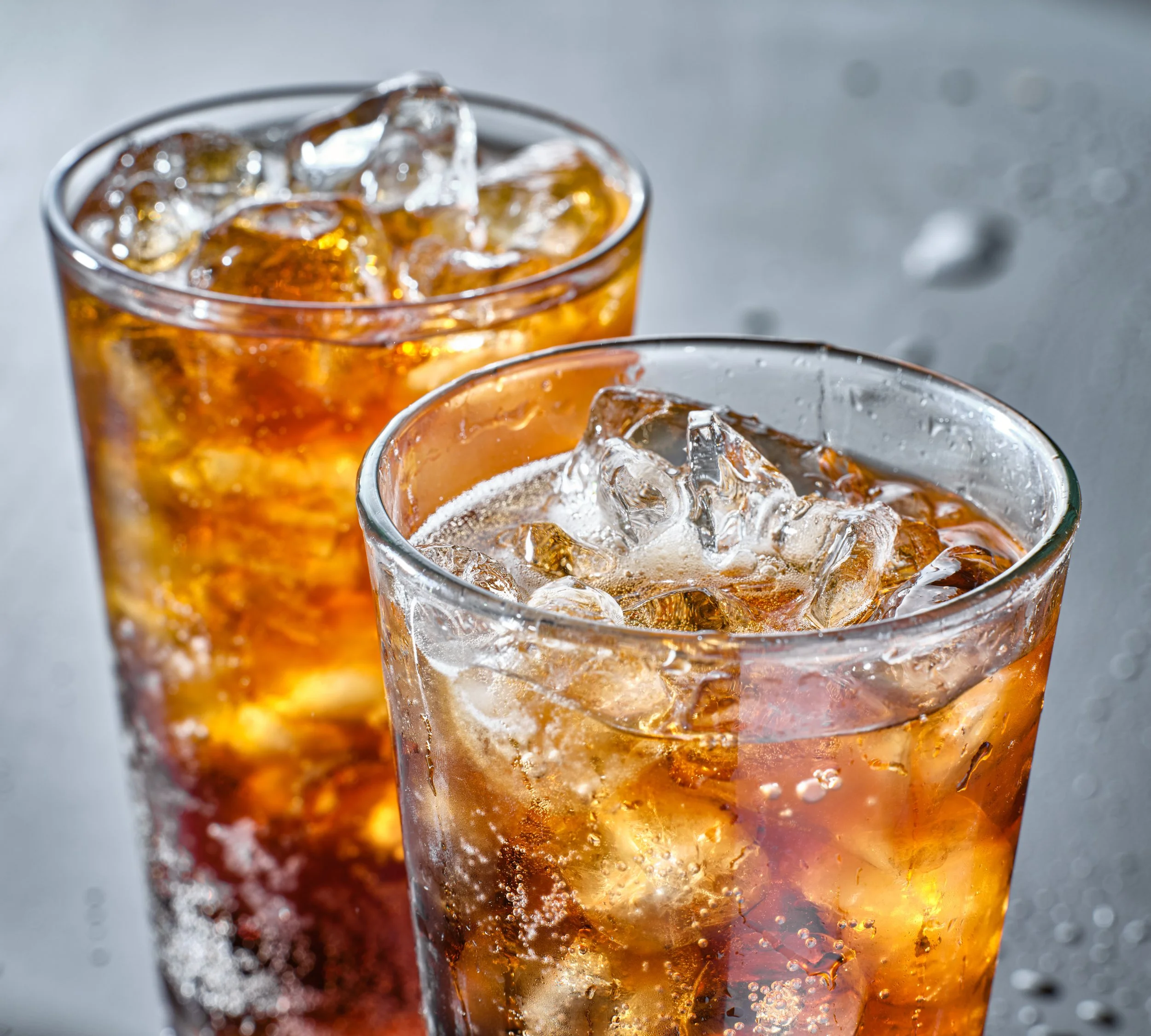 Two glasses of iced cola with ice cubes on a wet surface.