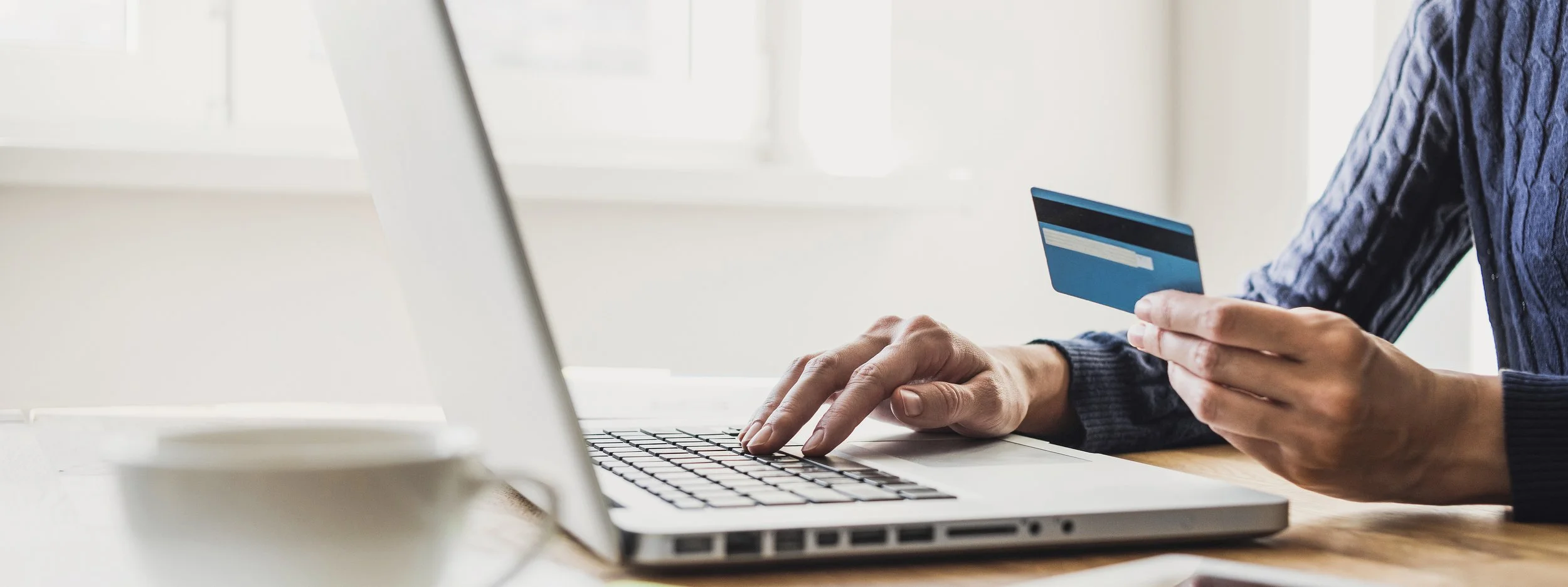 Person holding a credit card while using a laptop at a desk.