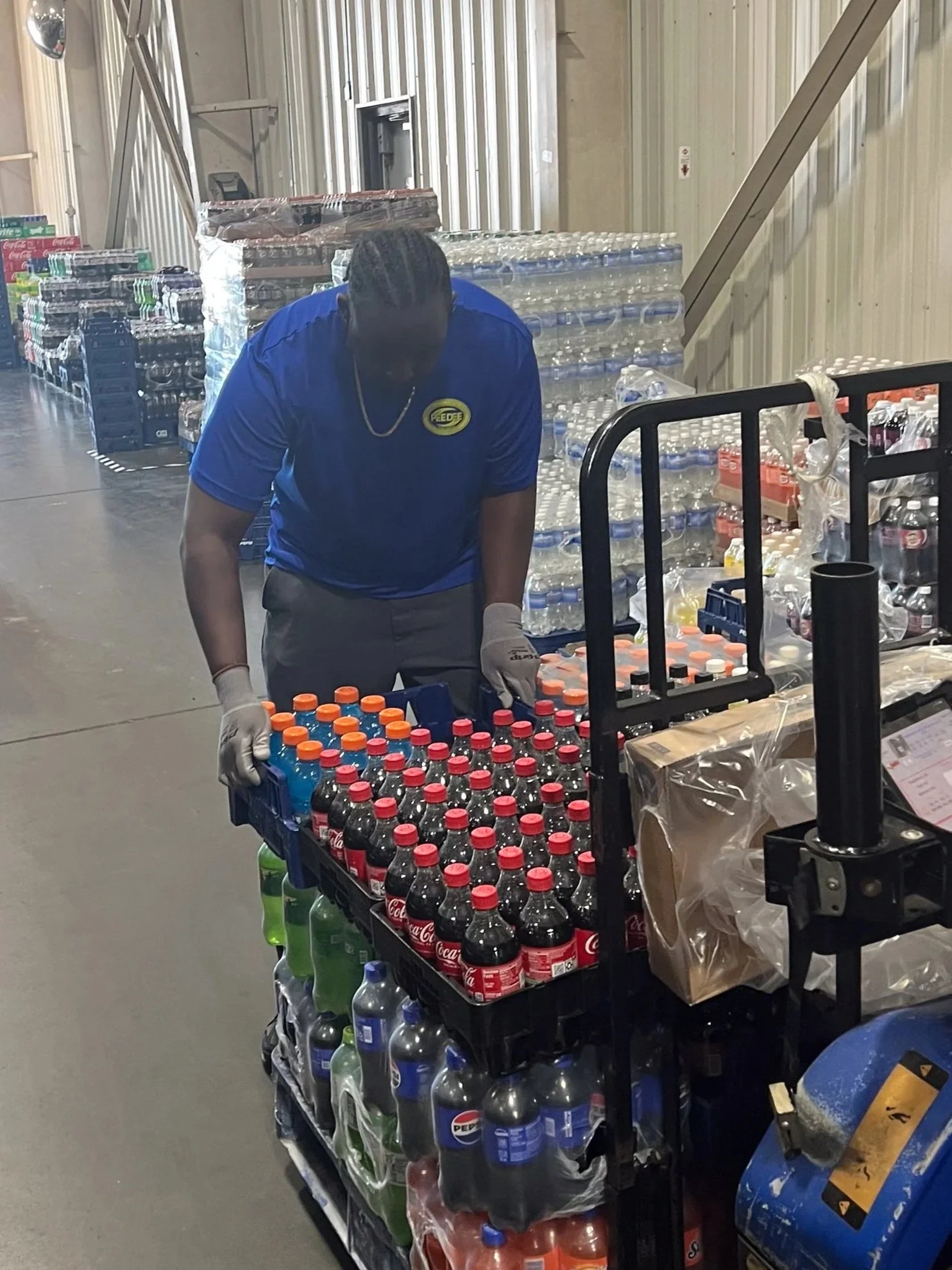 A worker arranges bottles of soda on a cart in a warehouse.