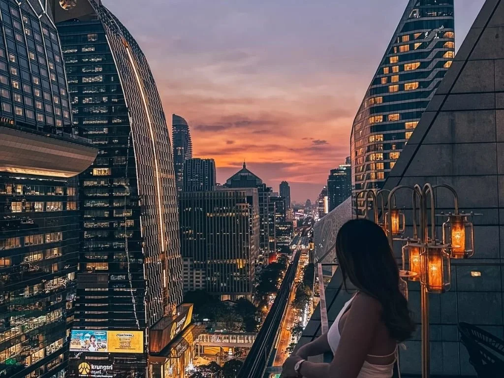 Guest taking in panoramic sunset views of the Bangkok skyline from an outdoor terrace at Rosewood Bangkok, Thailand.