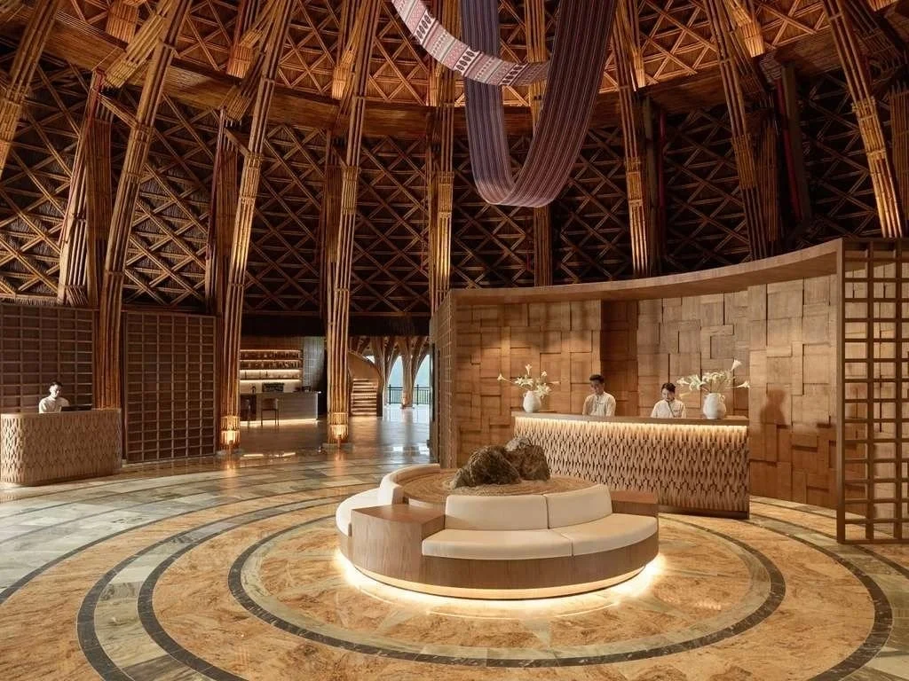 Interior of a hotel lobby with a wooden and brick design, a circular seating area in the center, and a reception desk with three staff members behind it.