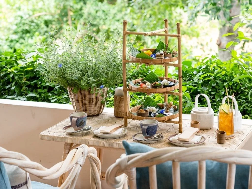 Artisanal northern Thai afternoon tea served on a tiered bamboo stand on an open-air veranda at Raya Heritage in Chiang Mai, Thailand.