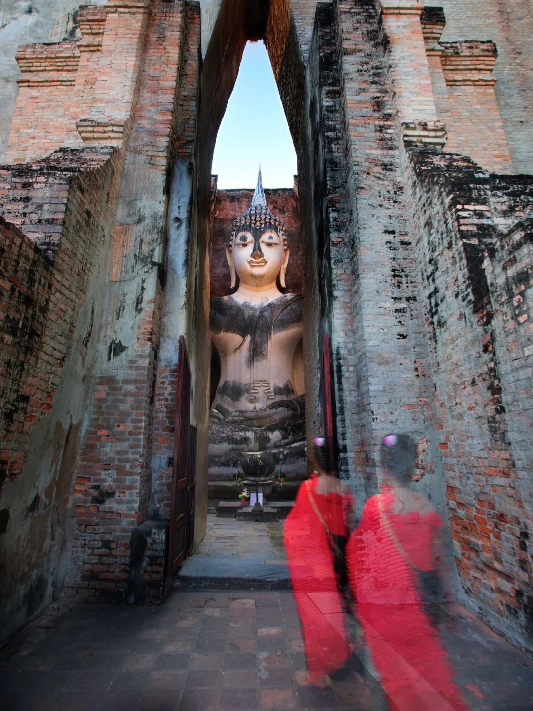 Colossal seated Phra Achana Buddha statue framed through the historic brick entryway of Wat Si Chum in Sukhothai, Thailand.