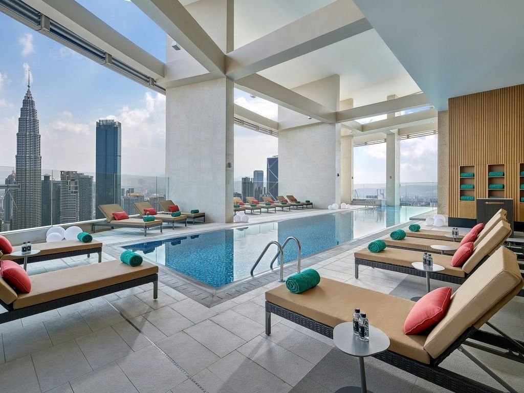 Indoor rooftop pool area with lounge chairs, green and red cushions, and a city skyline view including the Empire State Building in New York City.