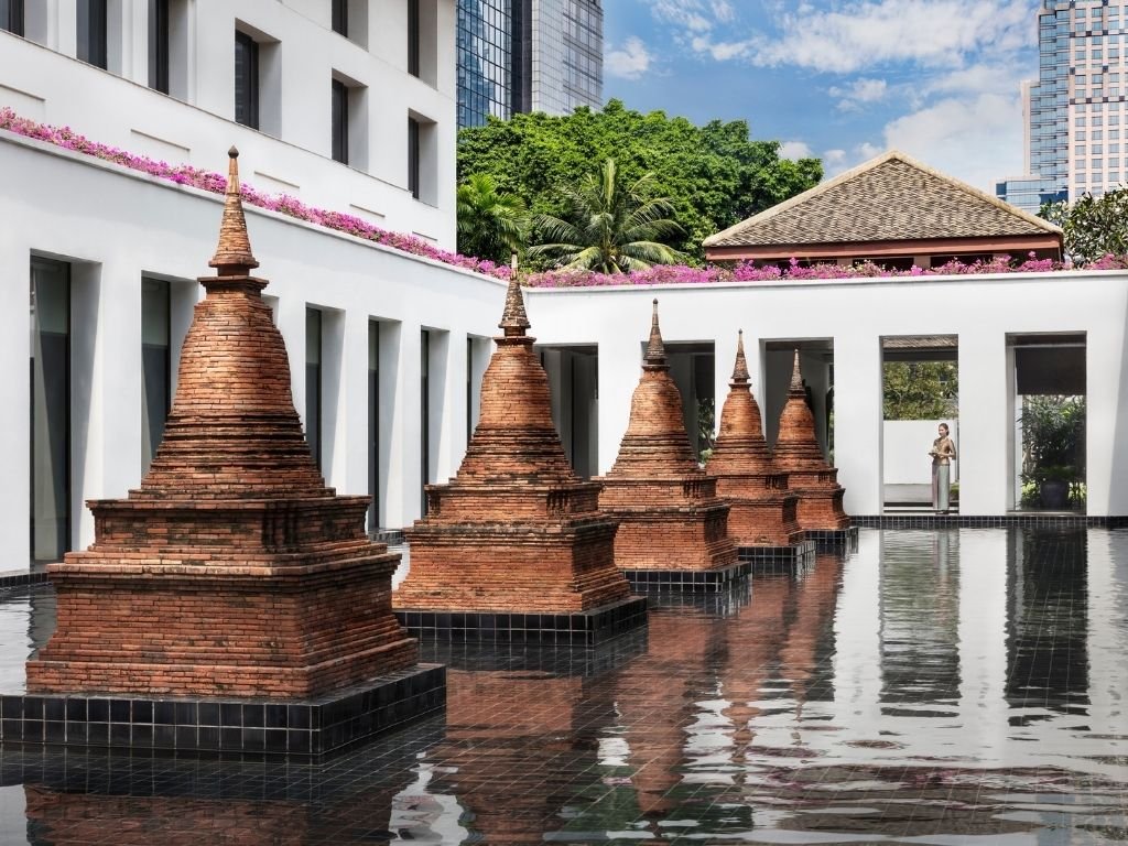 Historic red-brick Chedi stupas standing within a tranquil reflective pond courtyard at The Sukhothai Bangkok, Thailand.