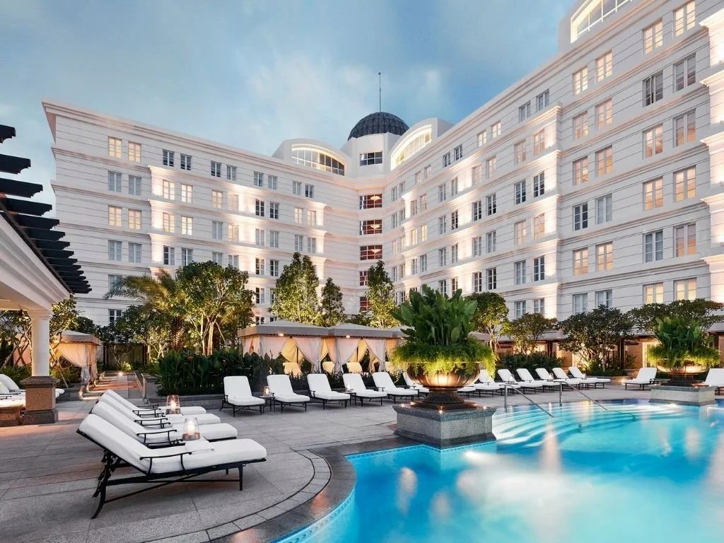 Illuminated French colonial facade and outdoor courtyard swimming pool with private cabanas at Park Hyatt Saigon in Ho Chi Minh City, Vietnam.