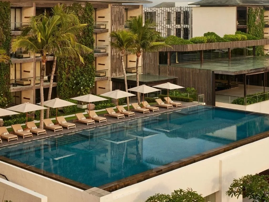Sun loungers and umbrellas along the oceanfront swimming pool framed by vertical gardens at Alila Seminyak in Bali, Indonesia.