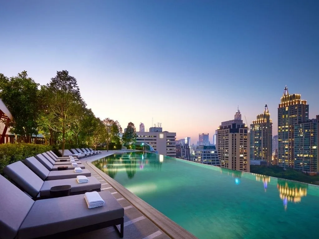 Rooftop infinity swimming pool and sun loungers overlooking the illuminated skyline at twilight at Park Hyatt Bangkok, Thailand.