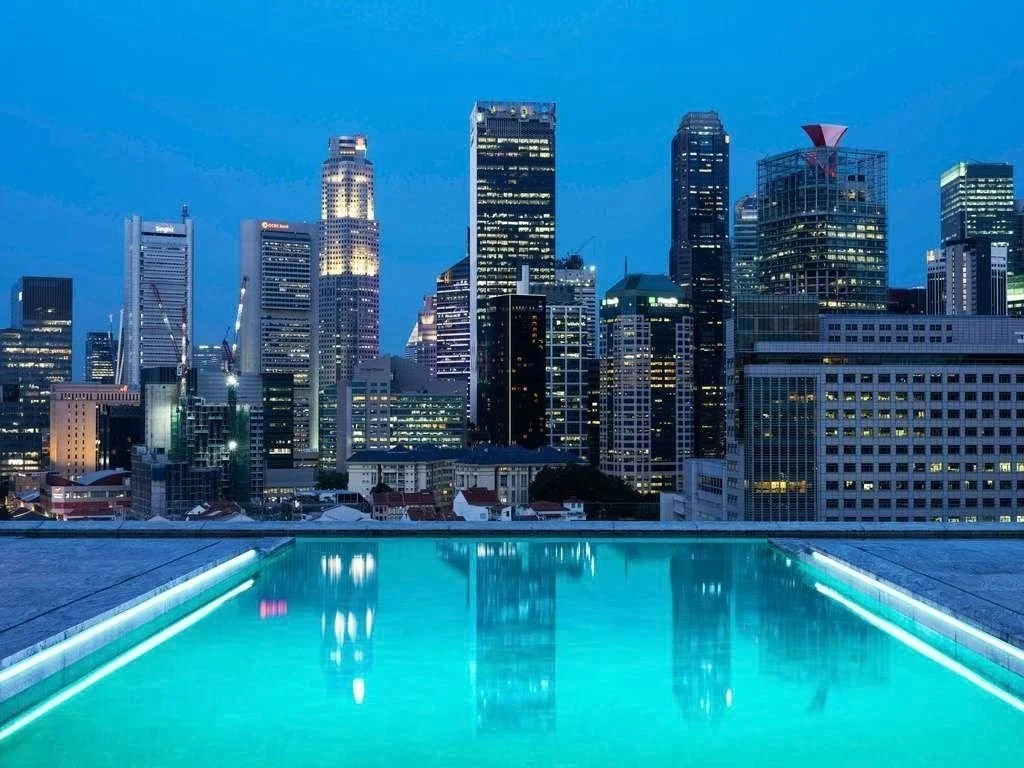 City skyline at night with illuminated skyscrapers viewed from a rooftop pool.
