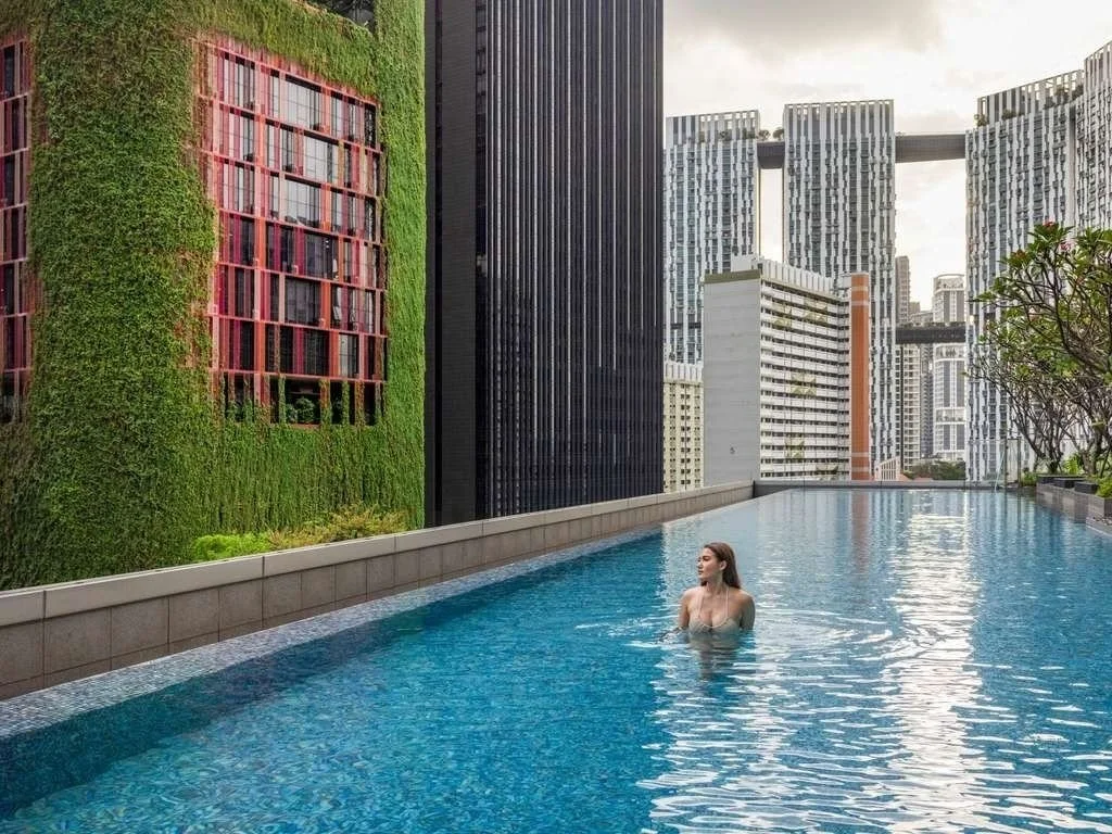 A woman swimming in a rooftop infinity pool surrounded by tall modern city buildings.
